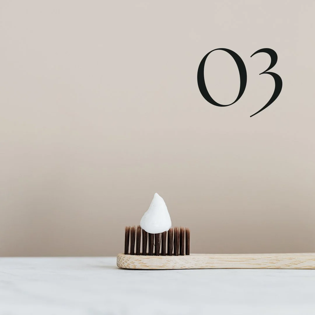 Image of a wooden toothbrush with white toothpaste on a marble countertop. 