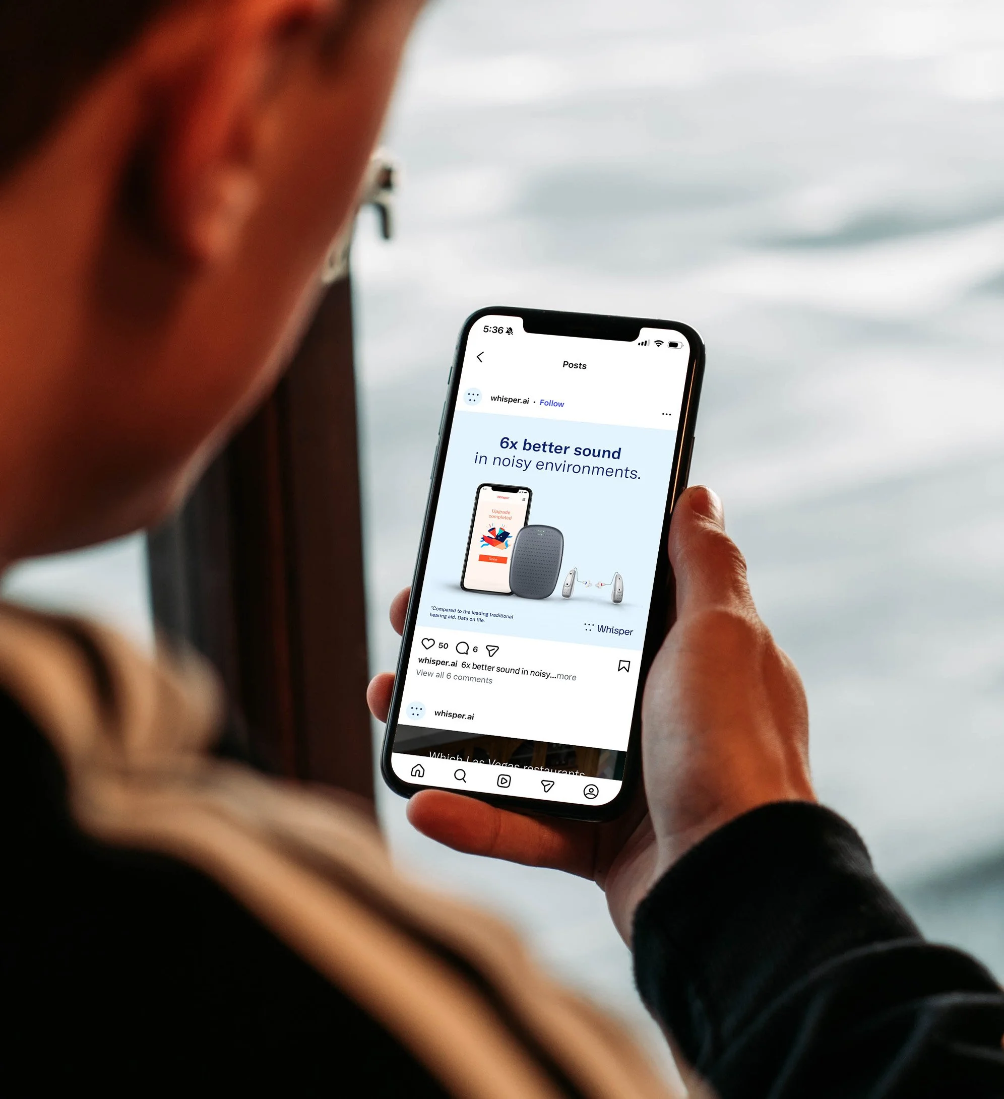 Man holding a cell phone, which shows a social media post for a hearing aid company.