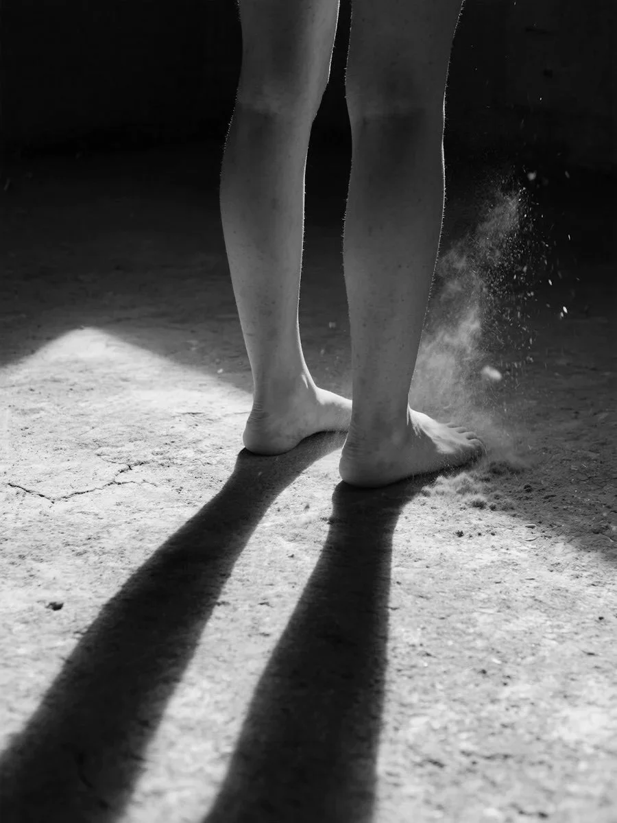 Close-up of person's legs and feet standing on dusty ground with long shadows and dust particles in the air.