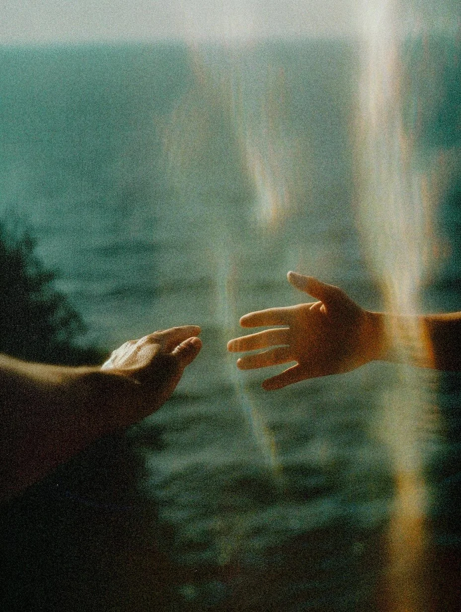 Two hands reaching out towards each other over a misty water surface with a hazy, serene background.