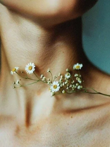 Close-up of a person's neck and collarbone with small white daisies decorated around the neck.
