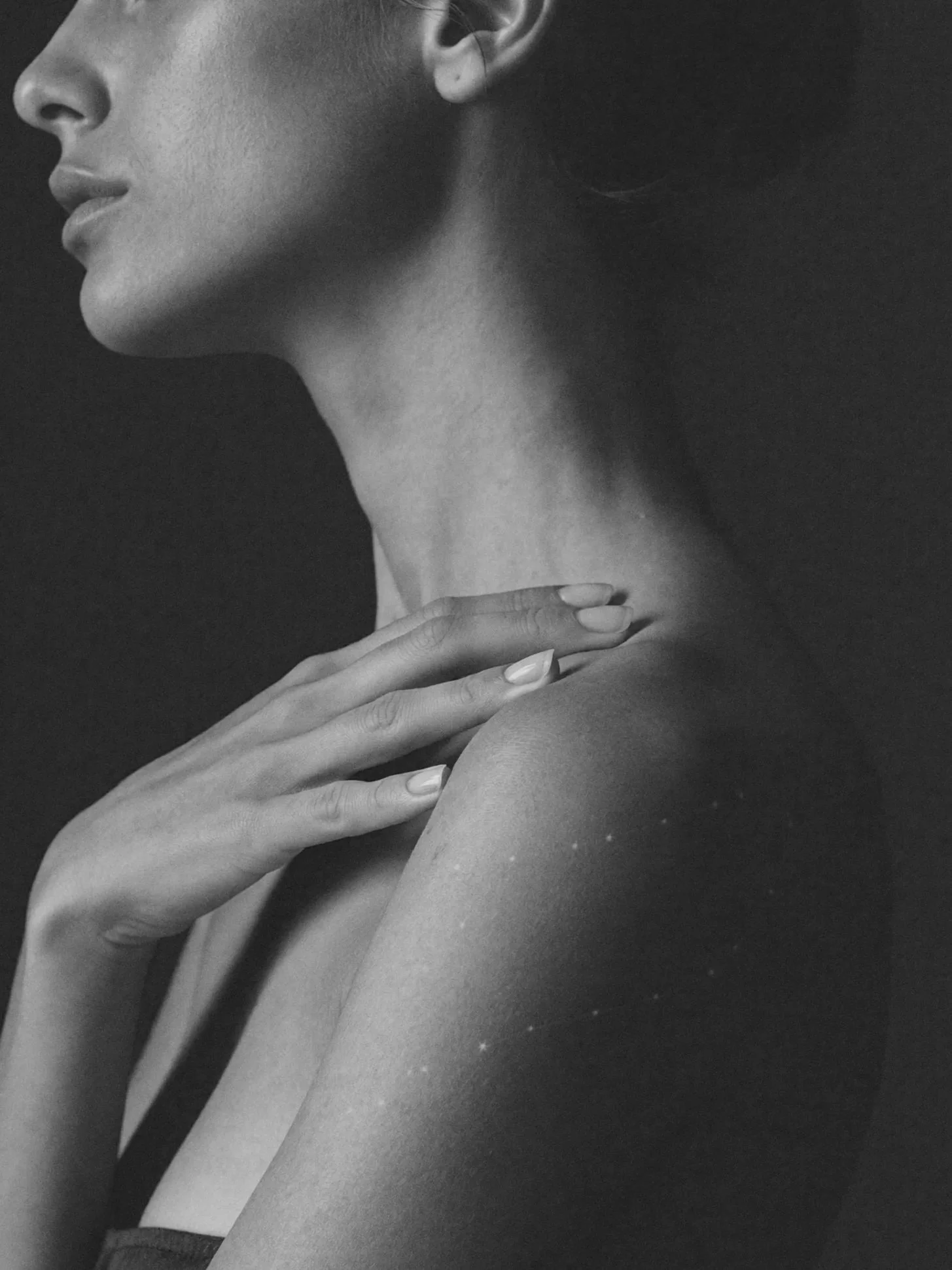 Close-up black and white photograph of a woman's face and hand, focusing on her lips, nose, neck, shoulder, and fingers resting on her shoulder.