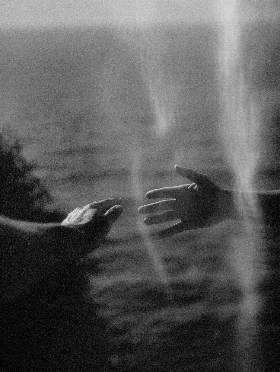 Two hands reaching towards each other through a foggy window, with light rays coming through, in black and white.
