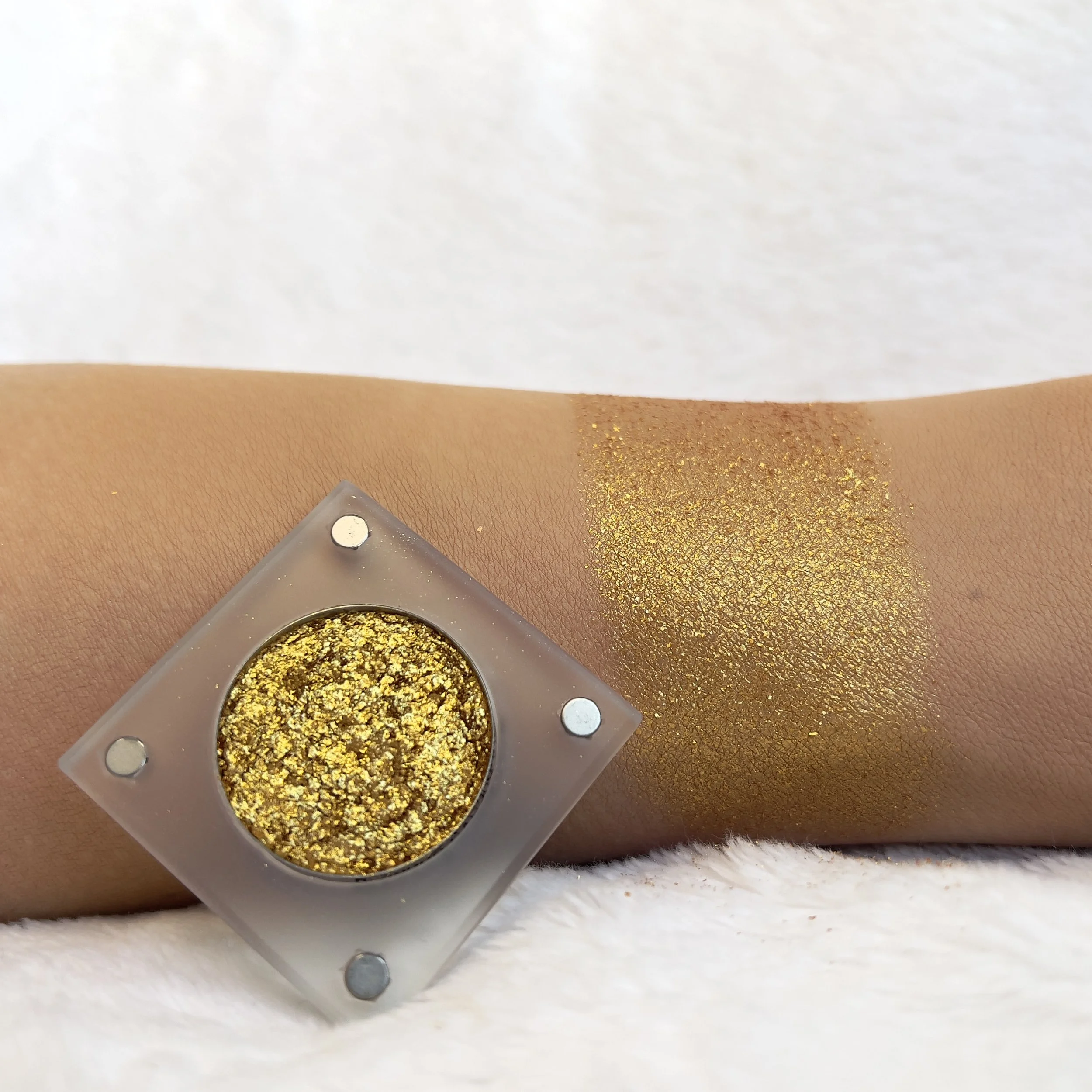 Radiant 21st by The Imperfectionist: rich antique gold glitter eyeshadow swatched on medium skin next to an open pan.