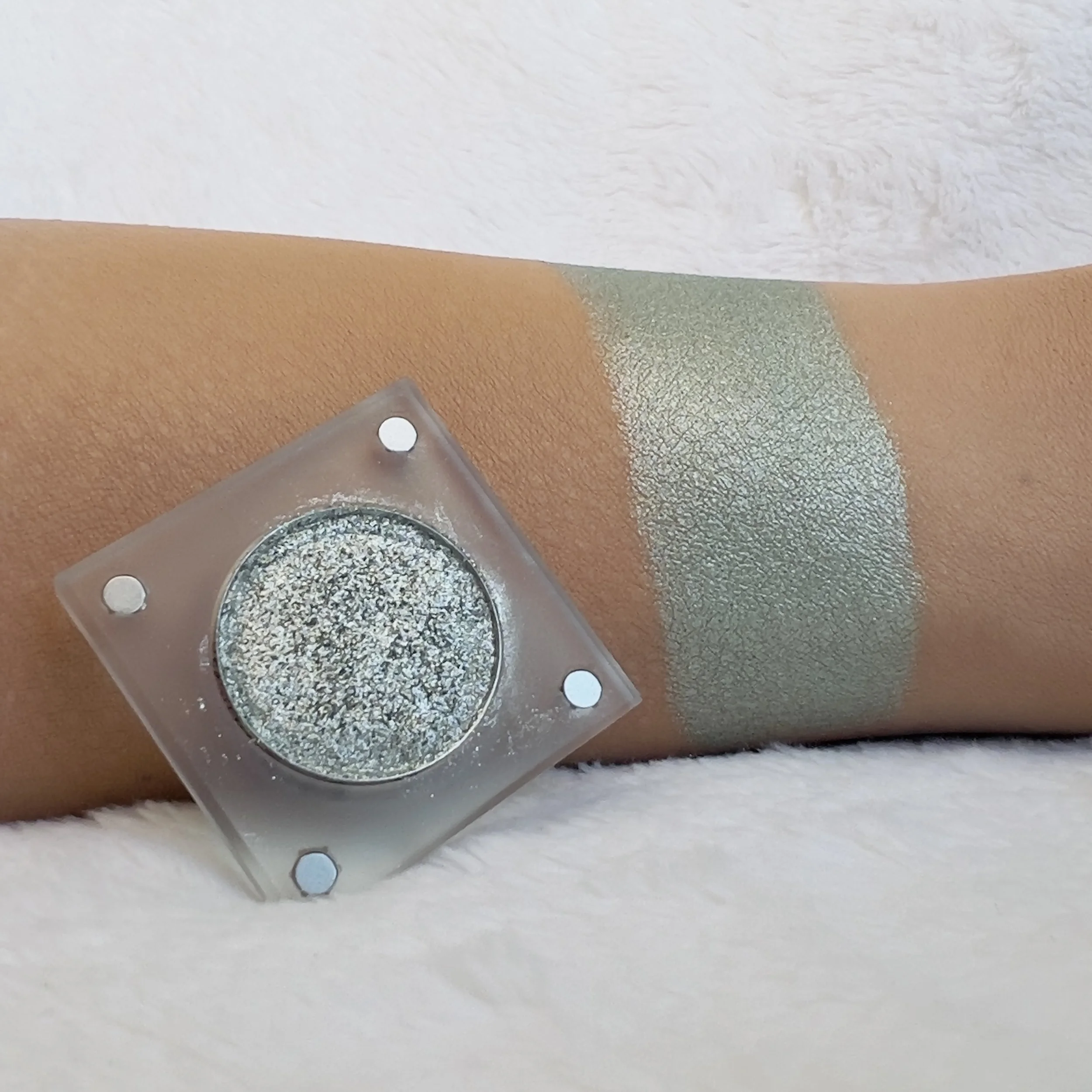Resilient Motion by The Imperfectionist: soft sage-green metallic eyeshadow swatched on medium skin beside an open pan.