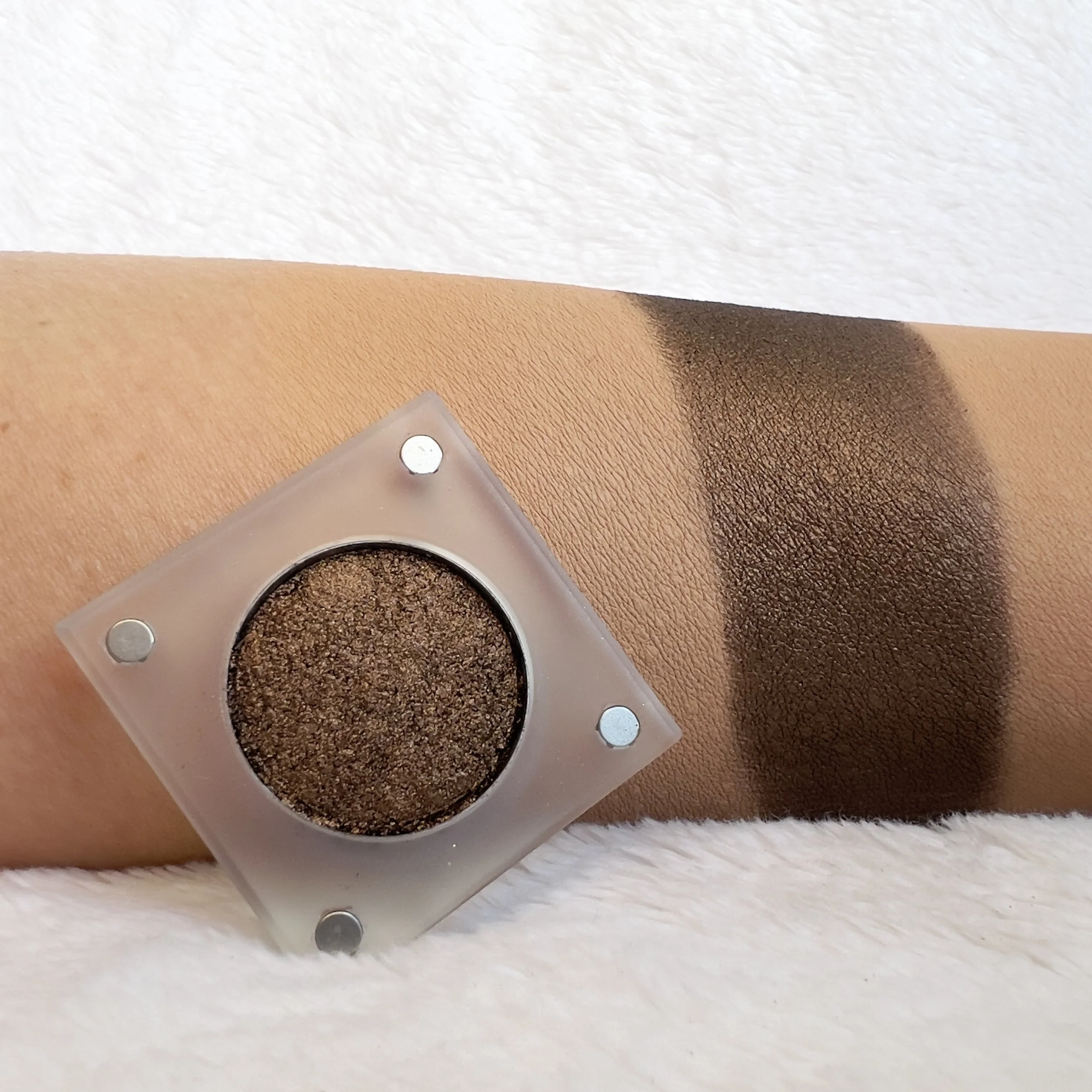 Restless Espresso by The Imperfectionist: deep bronzed brown shimmer eyeshadow swatched on medium skin next to an open pan.