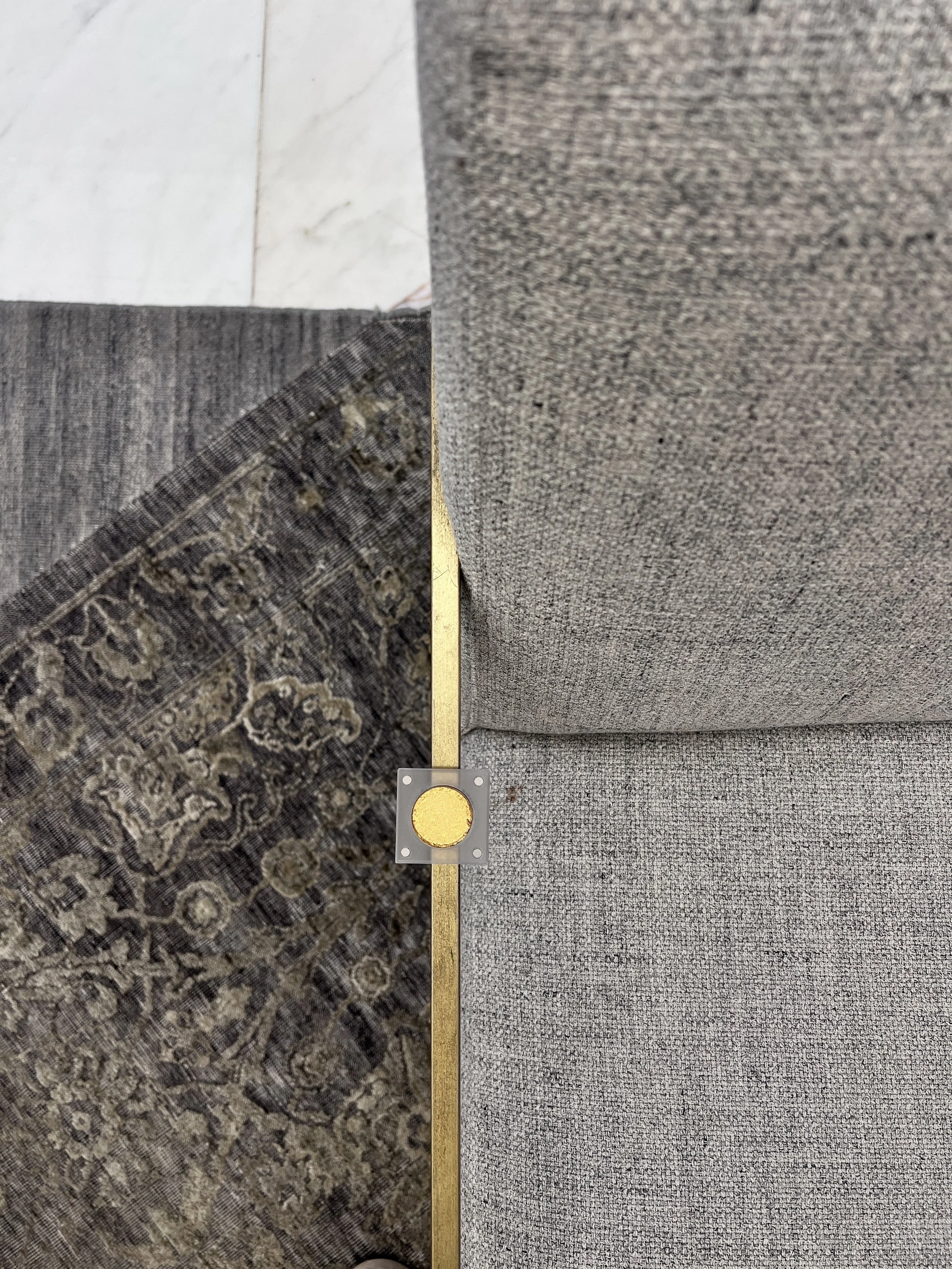 Radiant 21st, a warm gold eyeshadow, balanced on a brass table edge between a gray rug and linen sofa cushions.