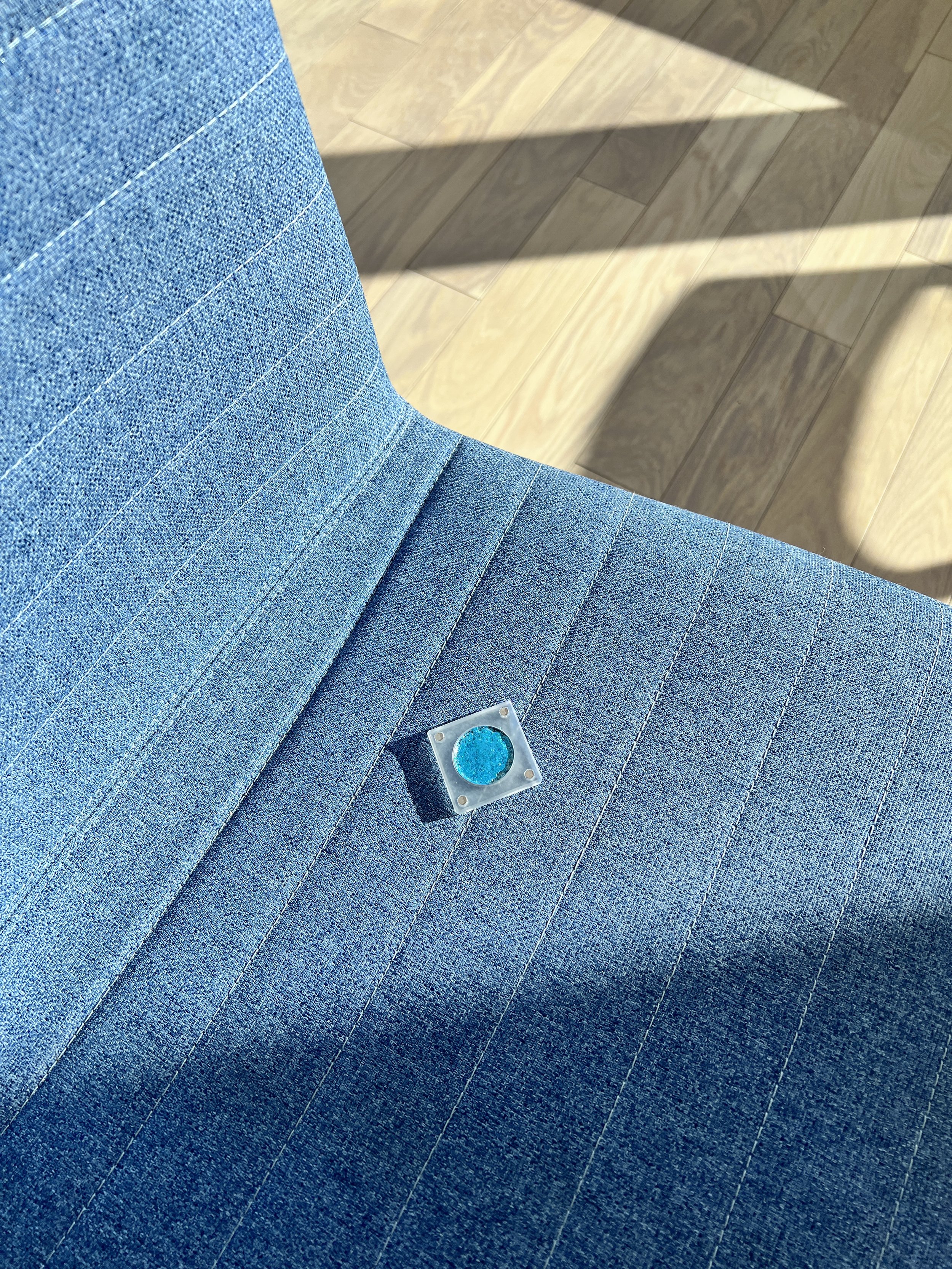 High-pigment blue metallic eyeshadow named Breathtaking Glow on sofa with jeans pattern in transparent magnetic case.