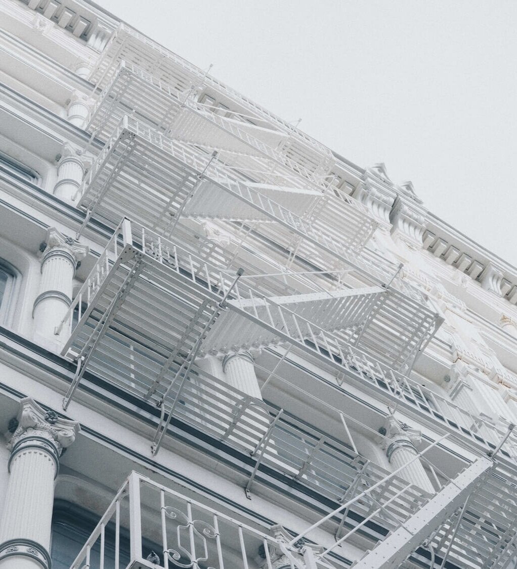 White facade of cast iron building with a series of columns and fire escapes all painted white