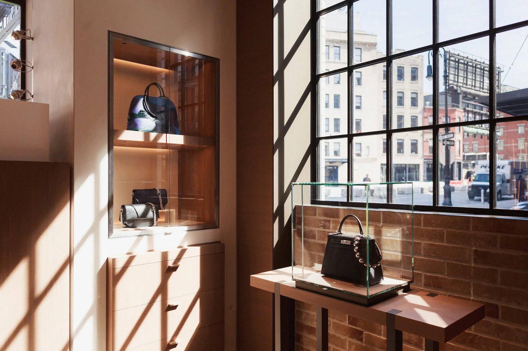 Retail displays of Hermes purses in New York City store with black mullions windows looking out to the city
