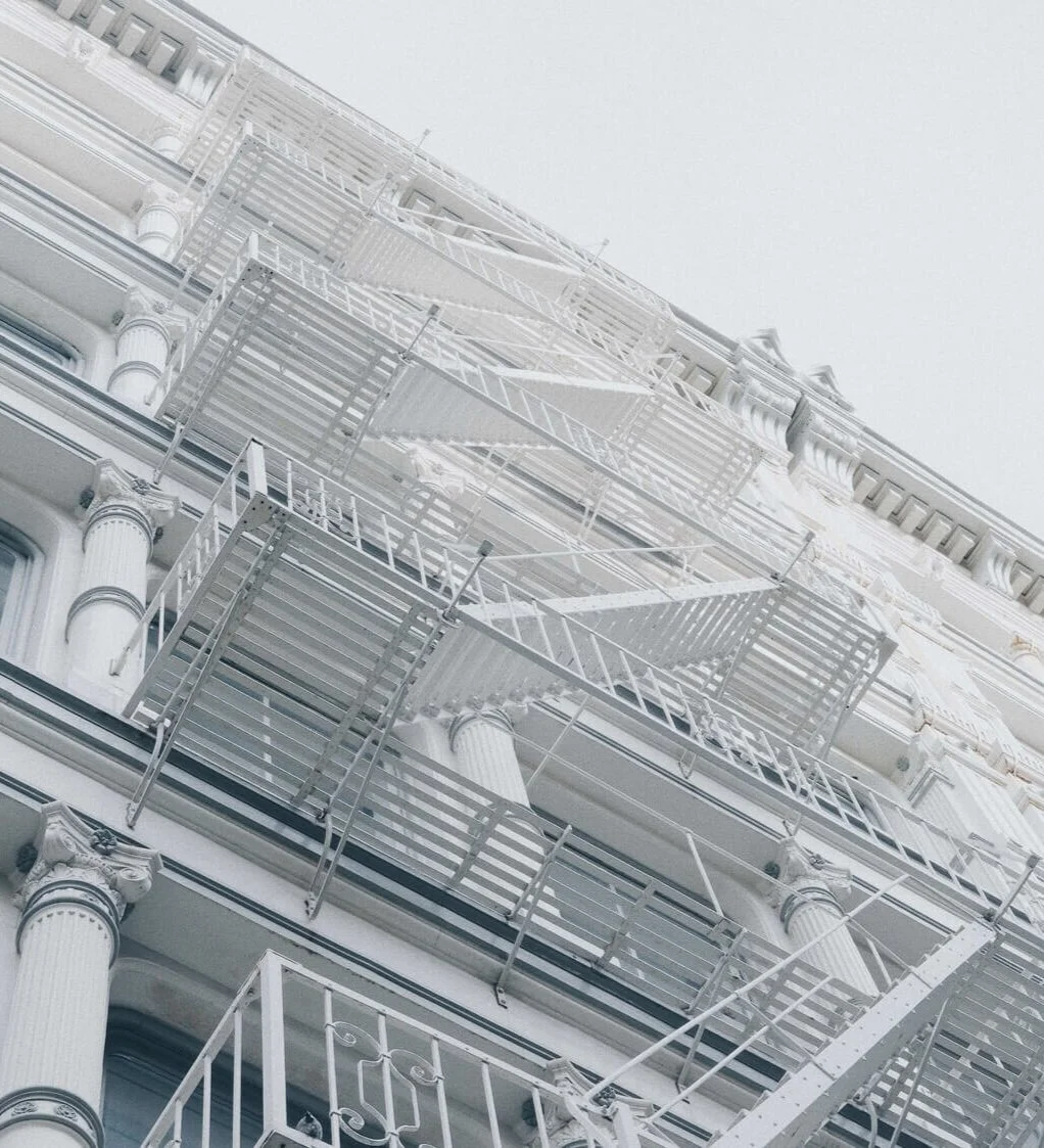 White facade of cast iron building with a series of columns and fire escapes all painted white