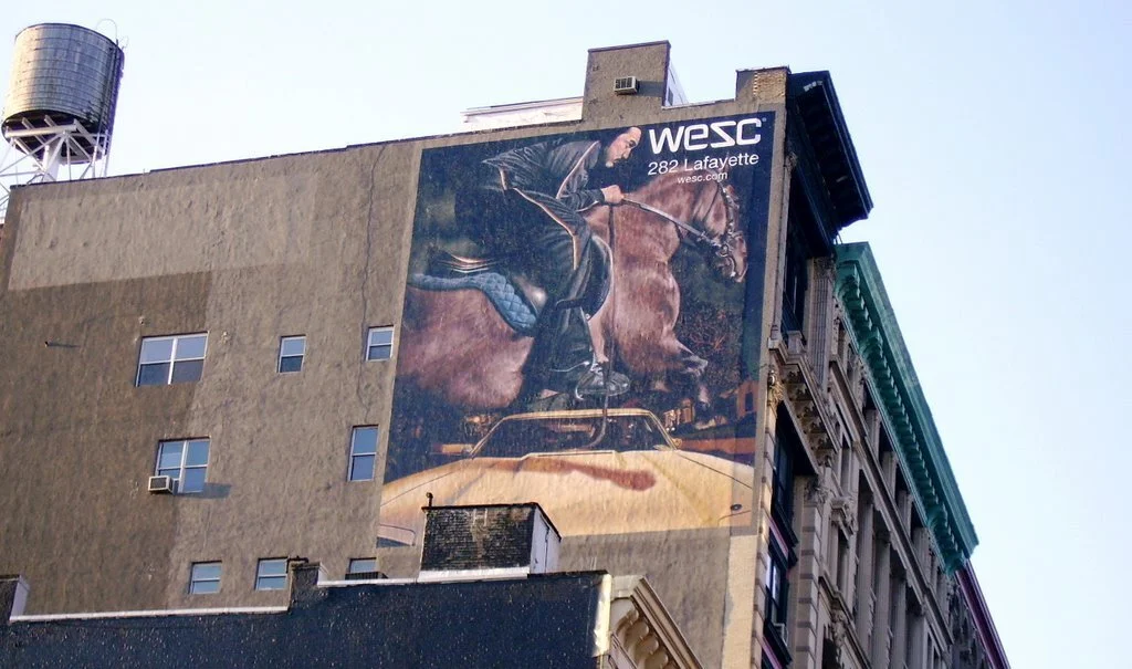 Advertising for WeSC on the side of a New York City building showing a man riding a horse and a yellow car