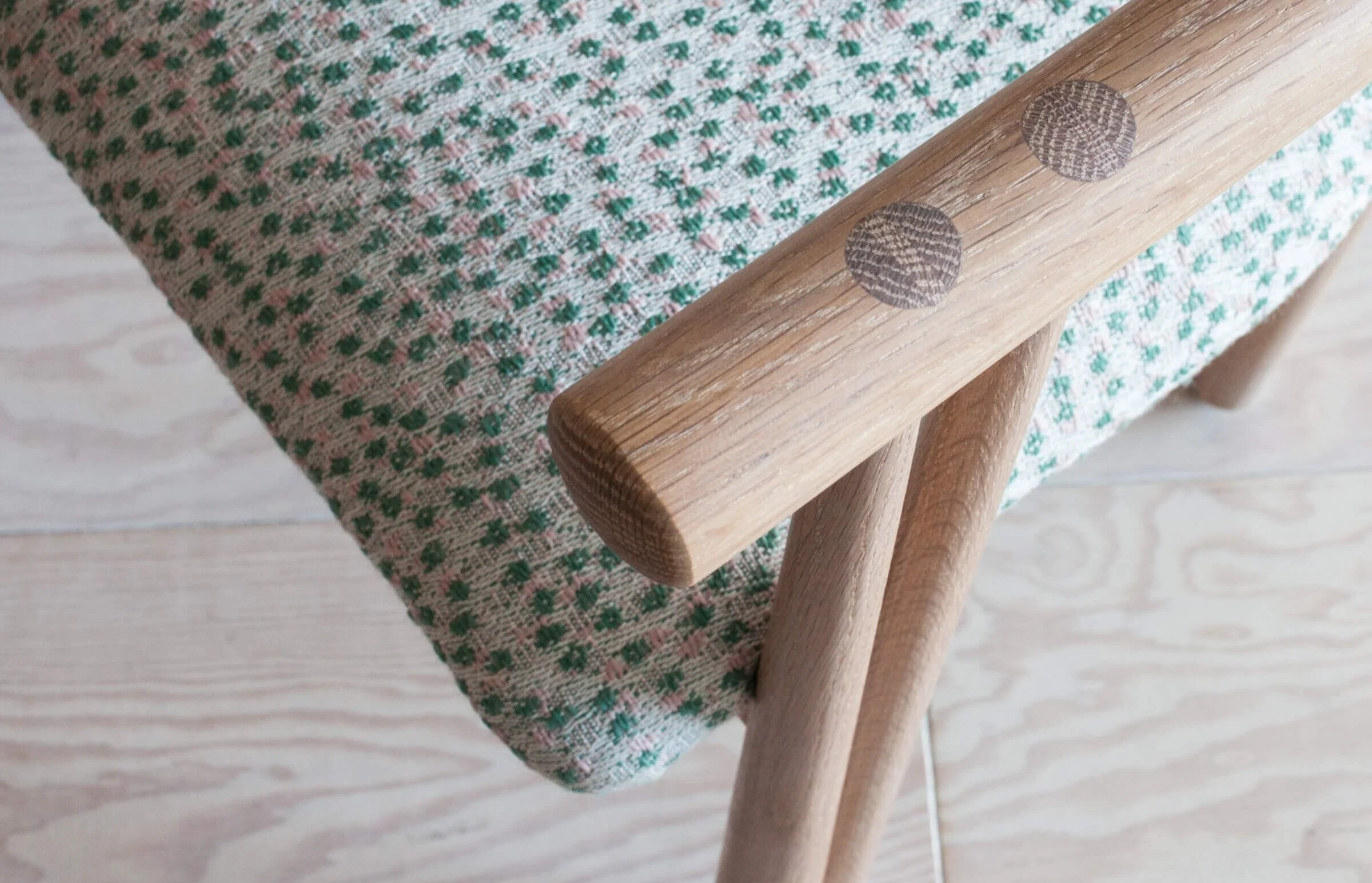 Detail of a wood chair arm with green and pink polka dot fabric design by De La Espada