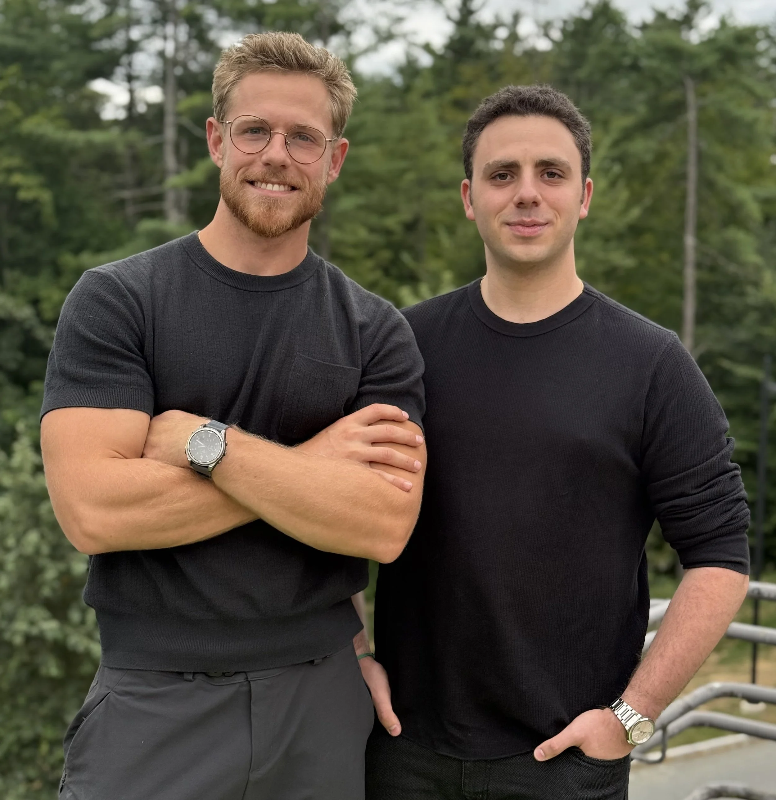 Peter and Levi standing outdoors in front of trees, both wearing black shirts and smiling