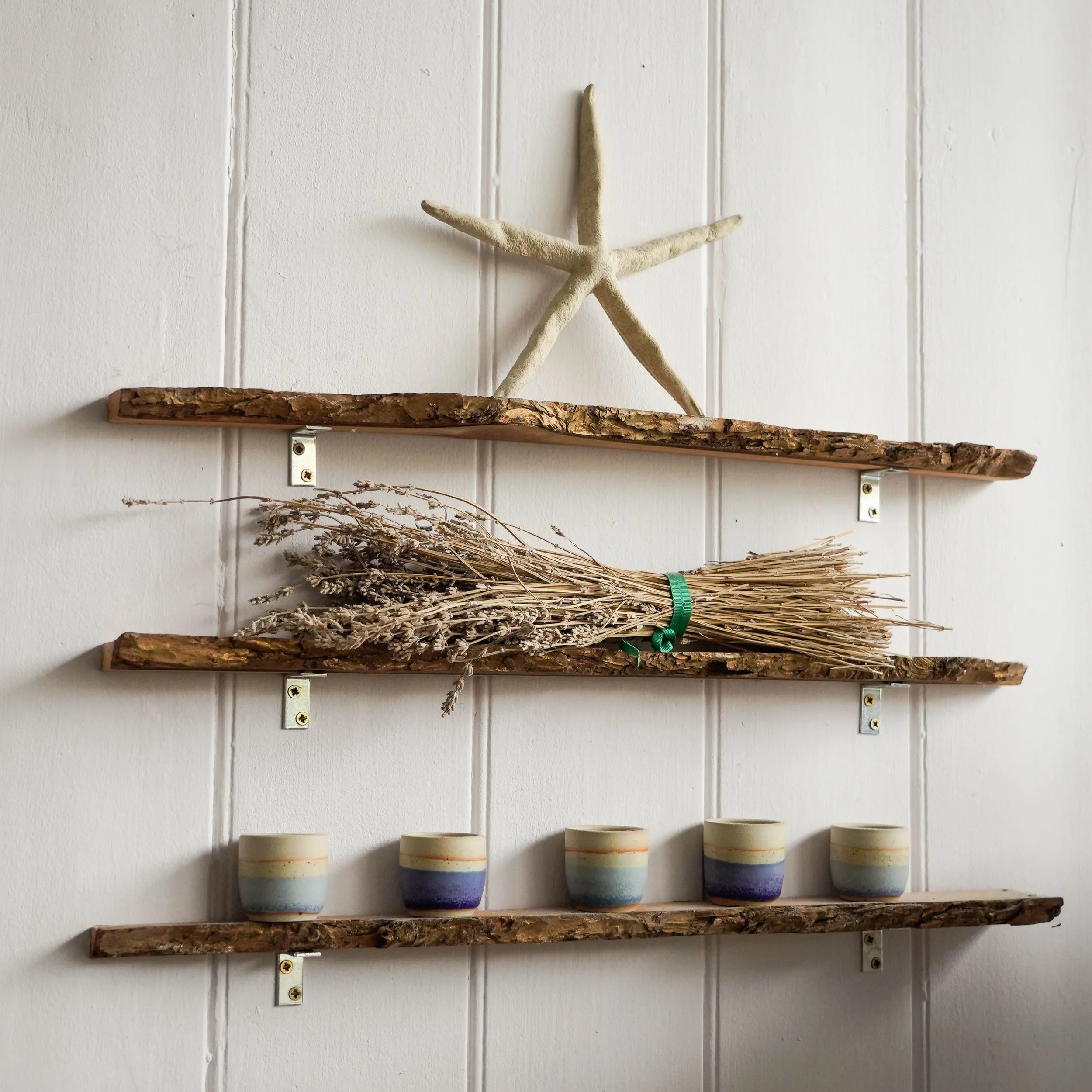 Decorative wall shelf with a starfish, dried lavender, and small ceramic cups against a white wall.