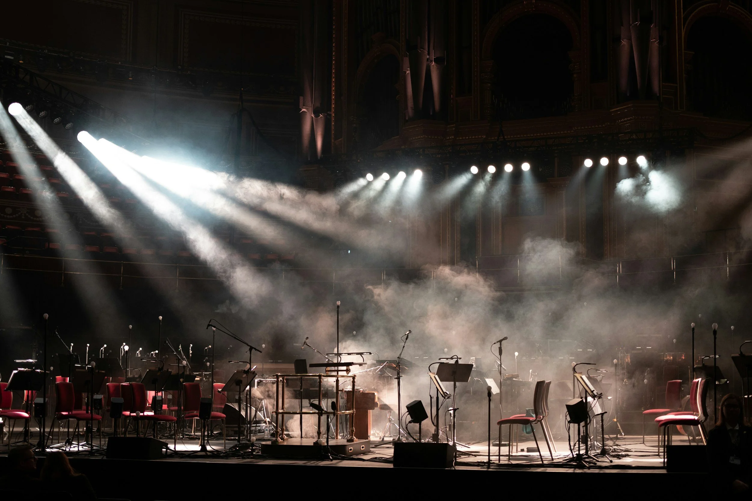 Empty stage set with chairs, music stands, and microphones in a concert hall with fog and dramatic lighting preparing for a performance.