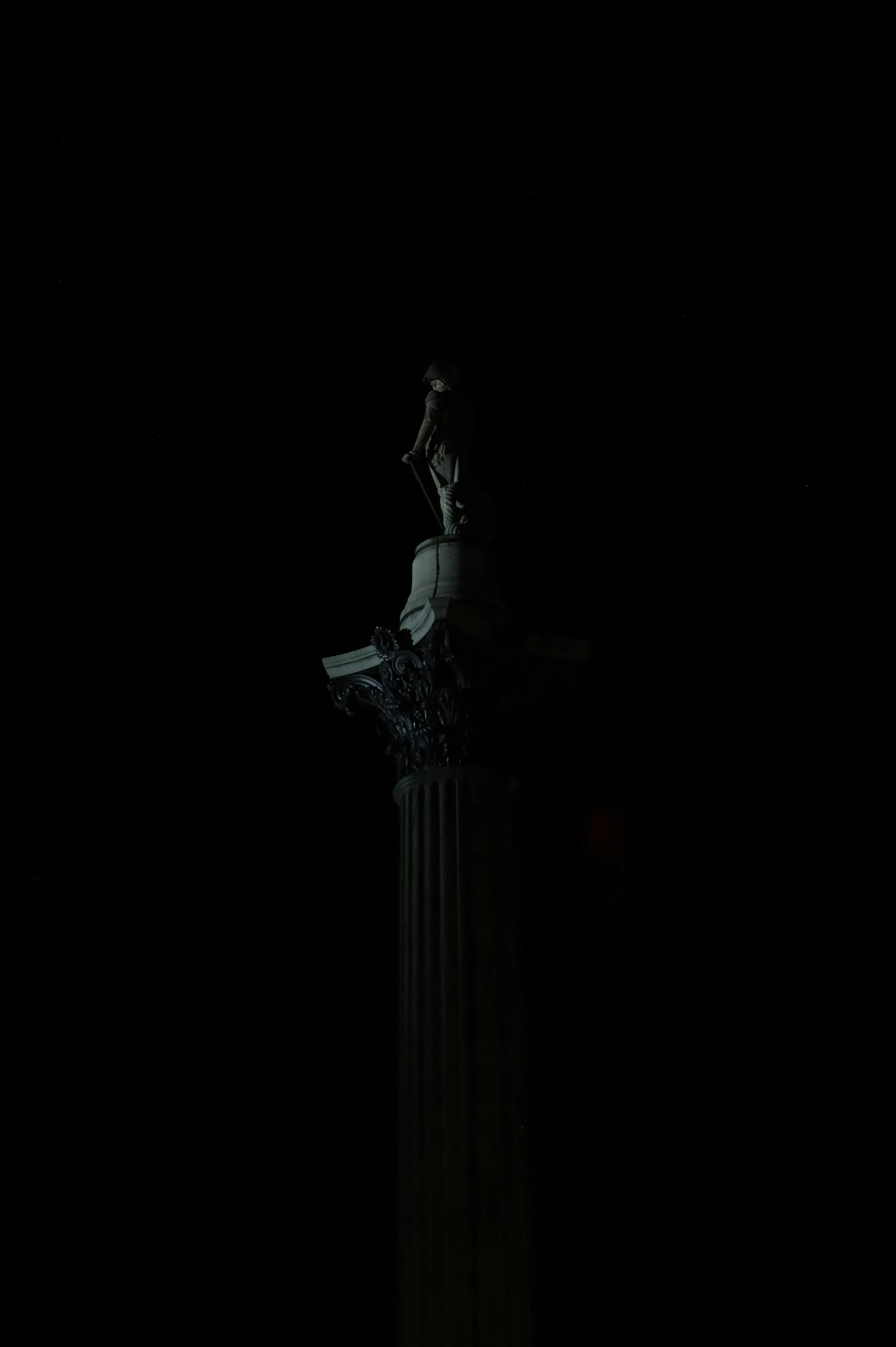 The image shows a dark sky with a statue on top of a tall, intricately decorated column. The statue appears to be a historical figure.