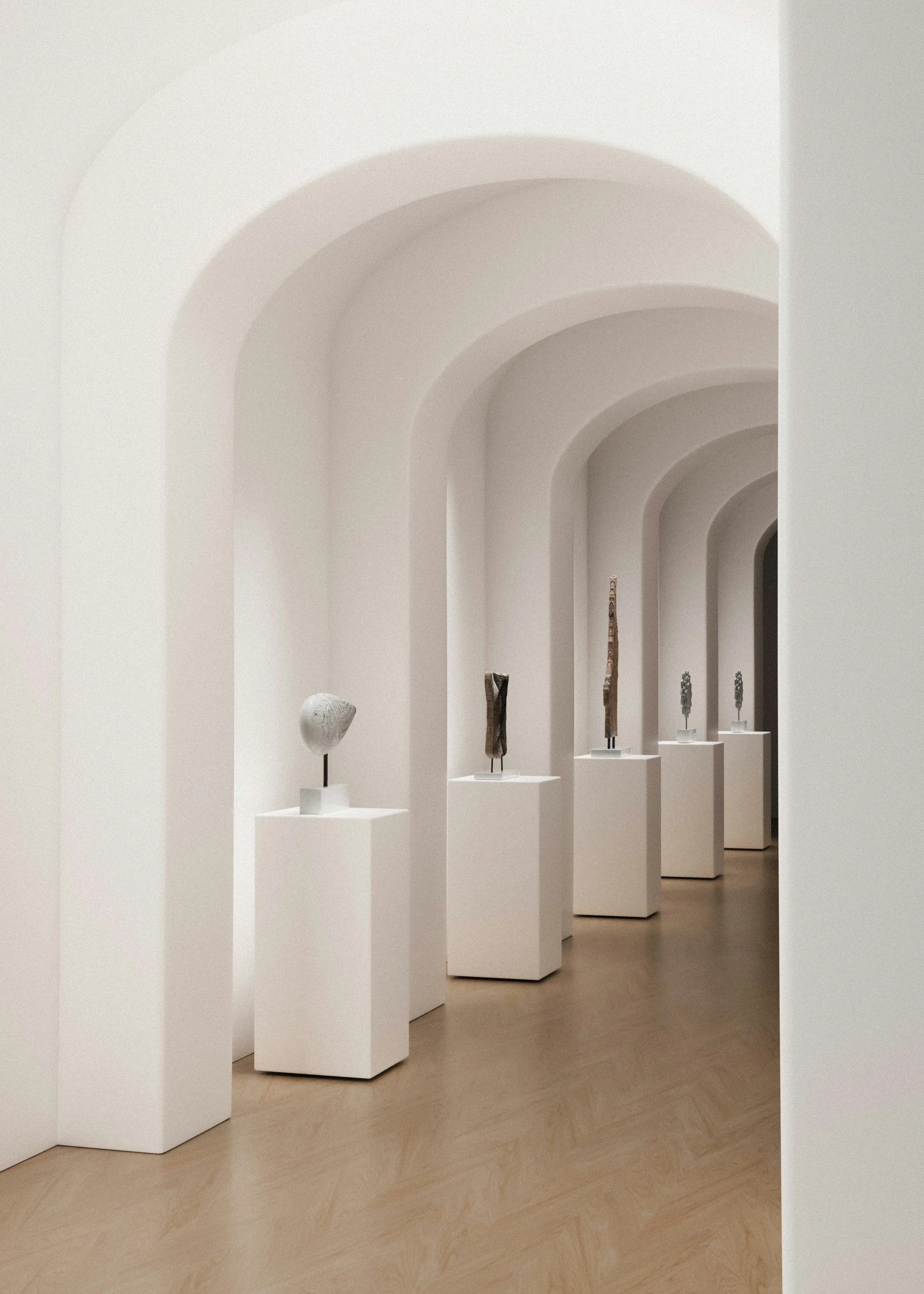 An art gallery displaying sculptures on white pedestals along a corridor with arched white walls and a wooden floor.