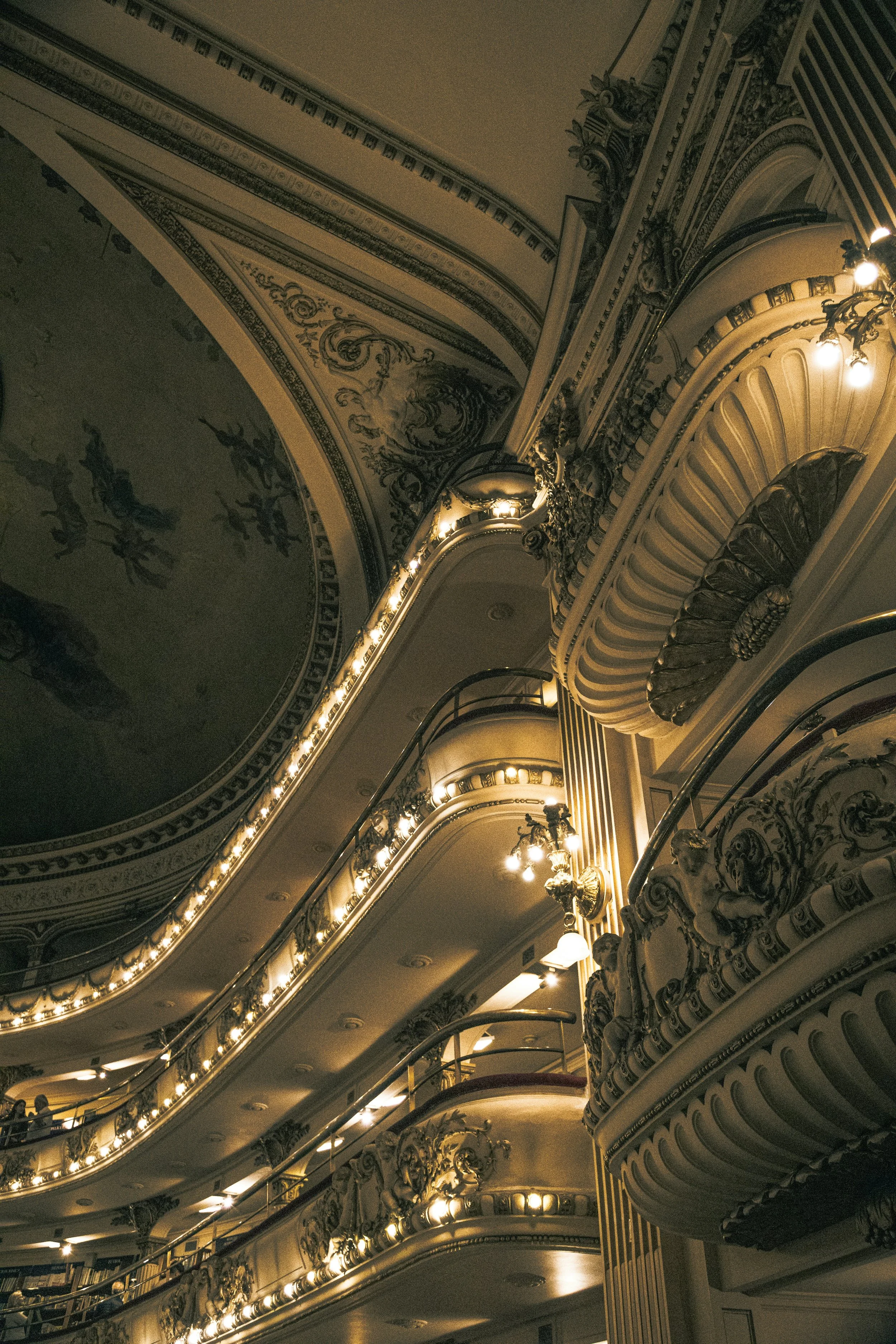 Interior view of an ornate theater or opera house with multiple balconies, decorative moldings, and elegant lighting fixtures, capturing a classic, luxurious atmosphere.