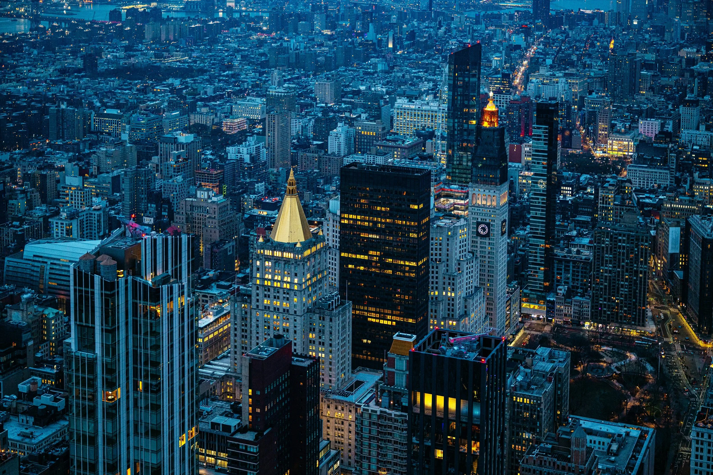 Aerial view of a cityscape at dusk with illuminated skyscrapers, including the MetLife Building and modern glass towers in New York City.