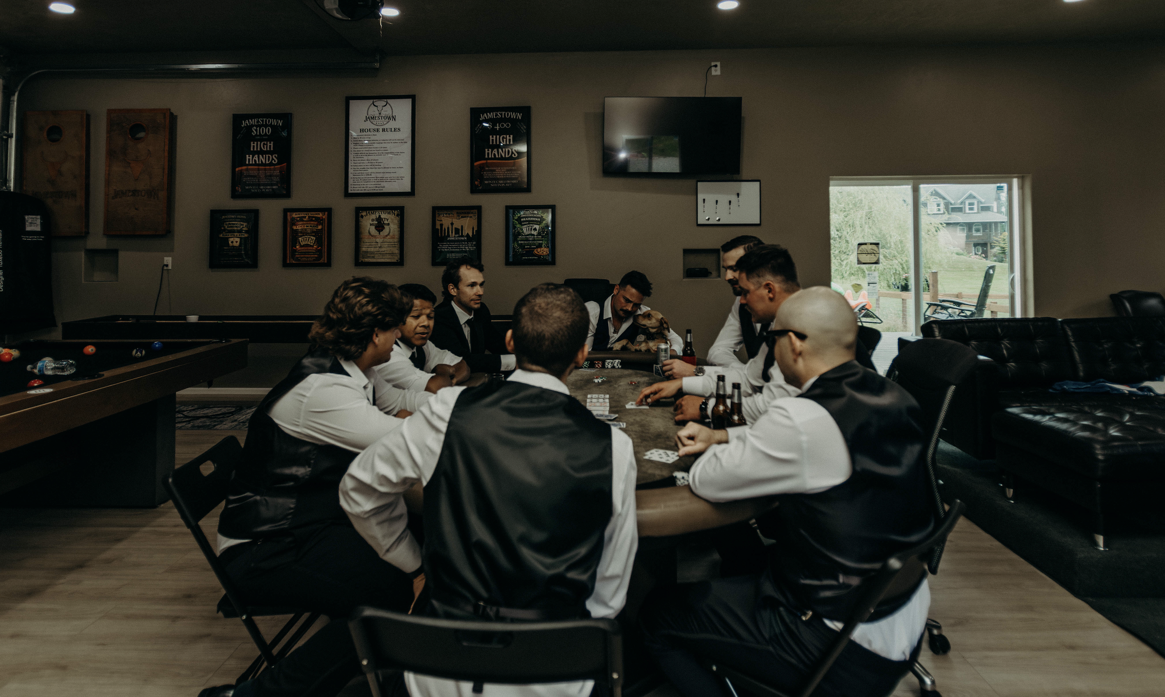 A group of people in formal attire playing poker around a table in a recreational room.