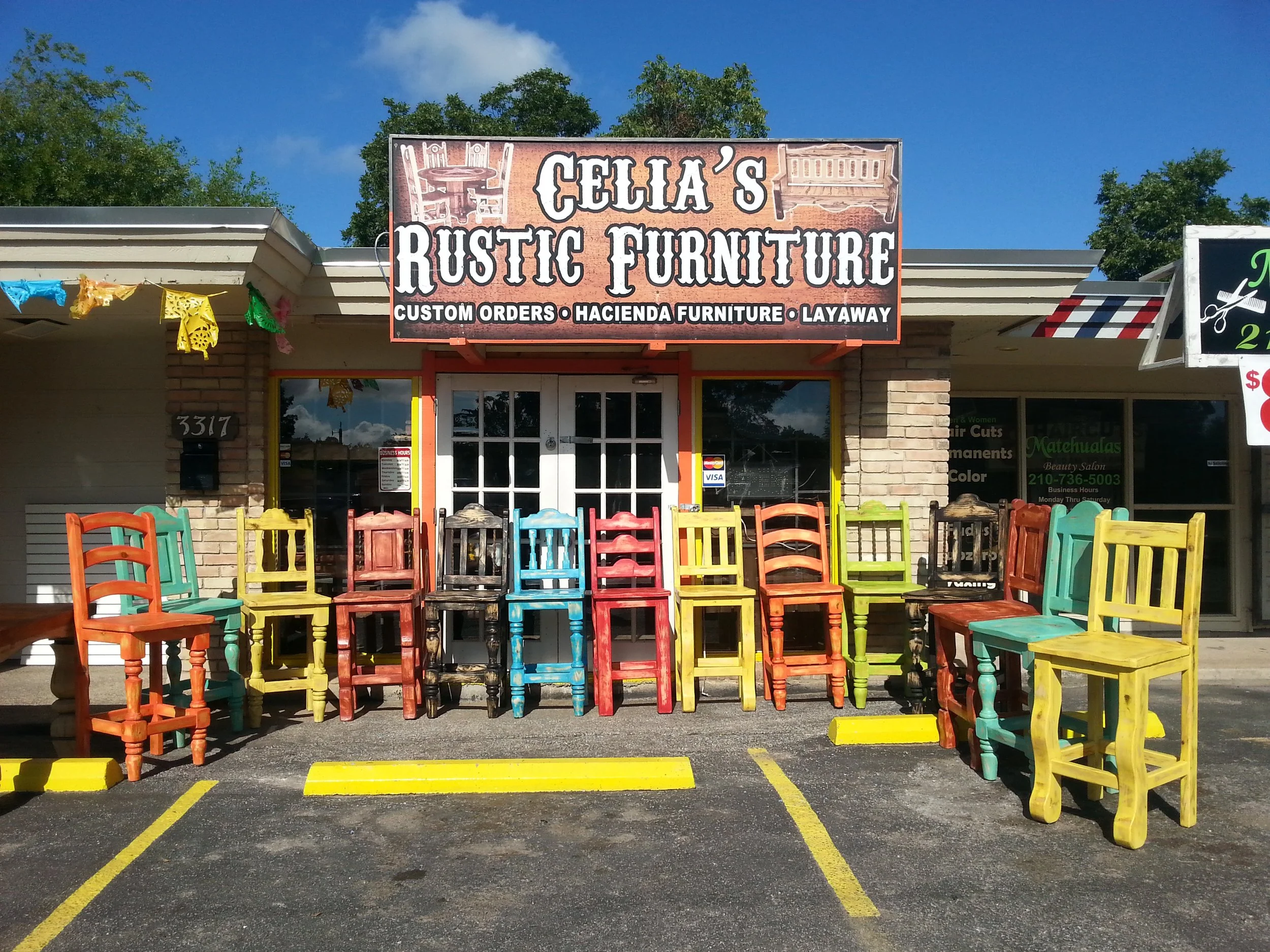 Storefront with a sign that reads 'Celia's Rustic Furniture' displaying colorful wooden chairs outside, with a blue sky and trees in the background.