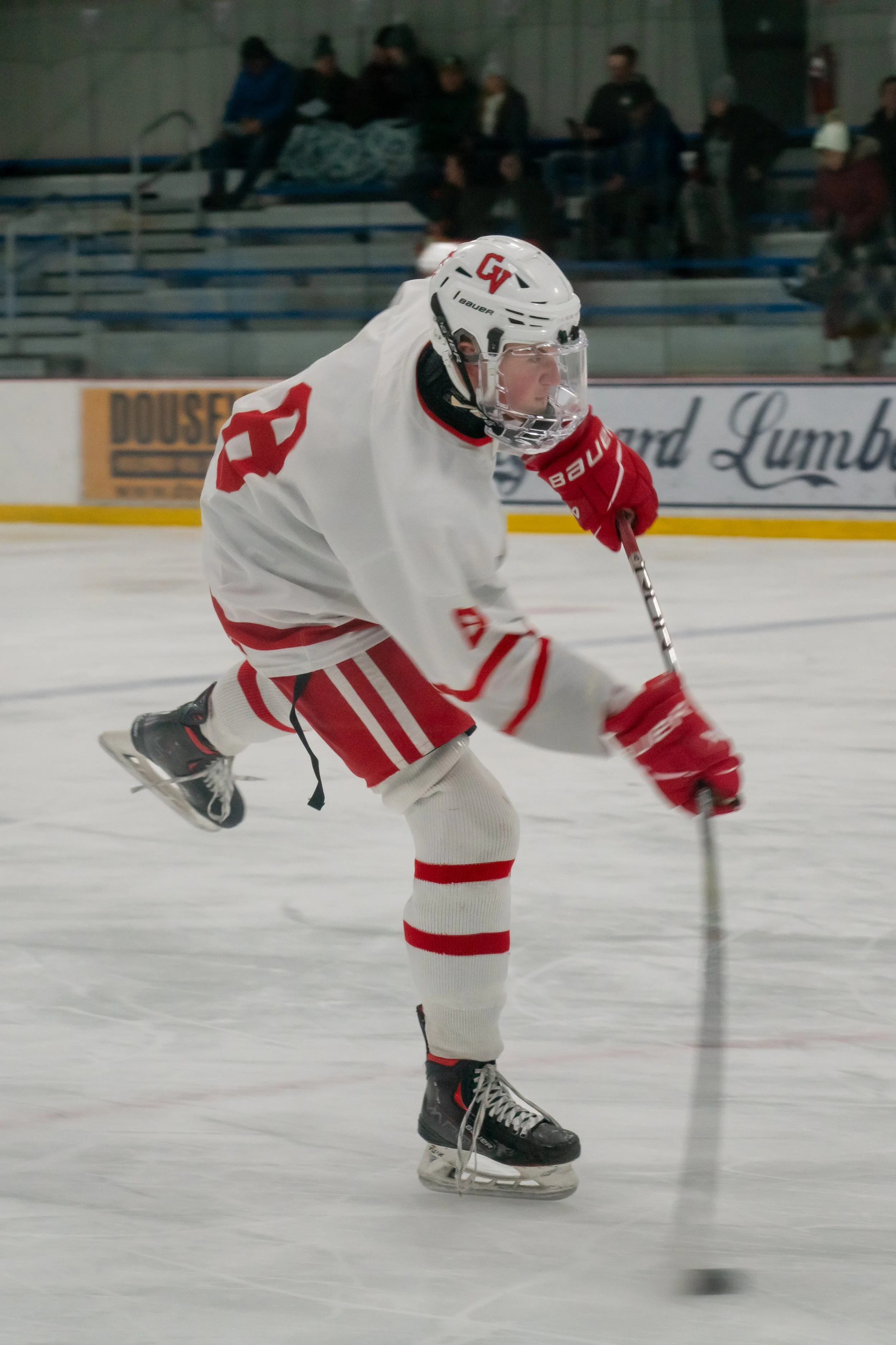 Ice hockey player wearing a white and red uniform, helmet, red gloves, and skates, focused on the puck on the ice rink.