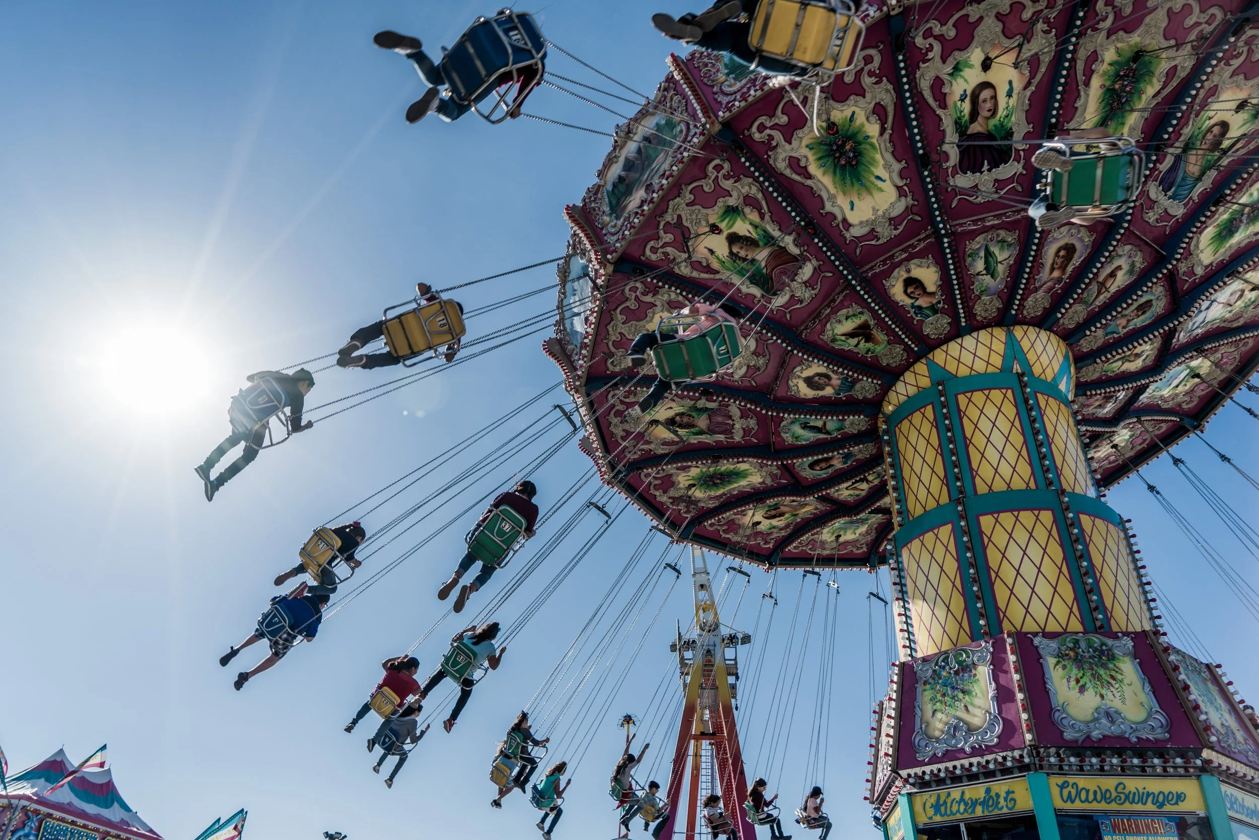 A colorful swing ride at an amusement park with riders swinging in the air against a bright blue sky and the sun shining.
