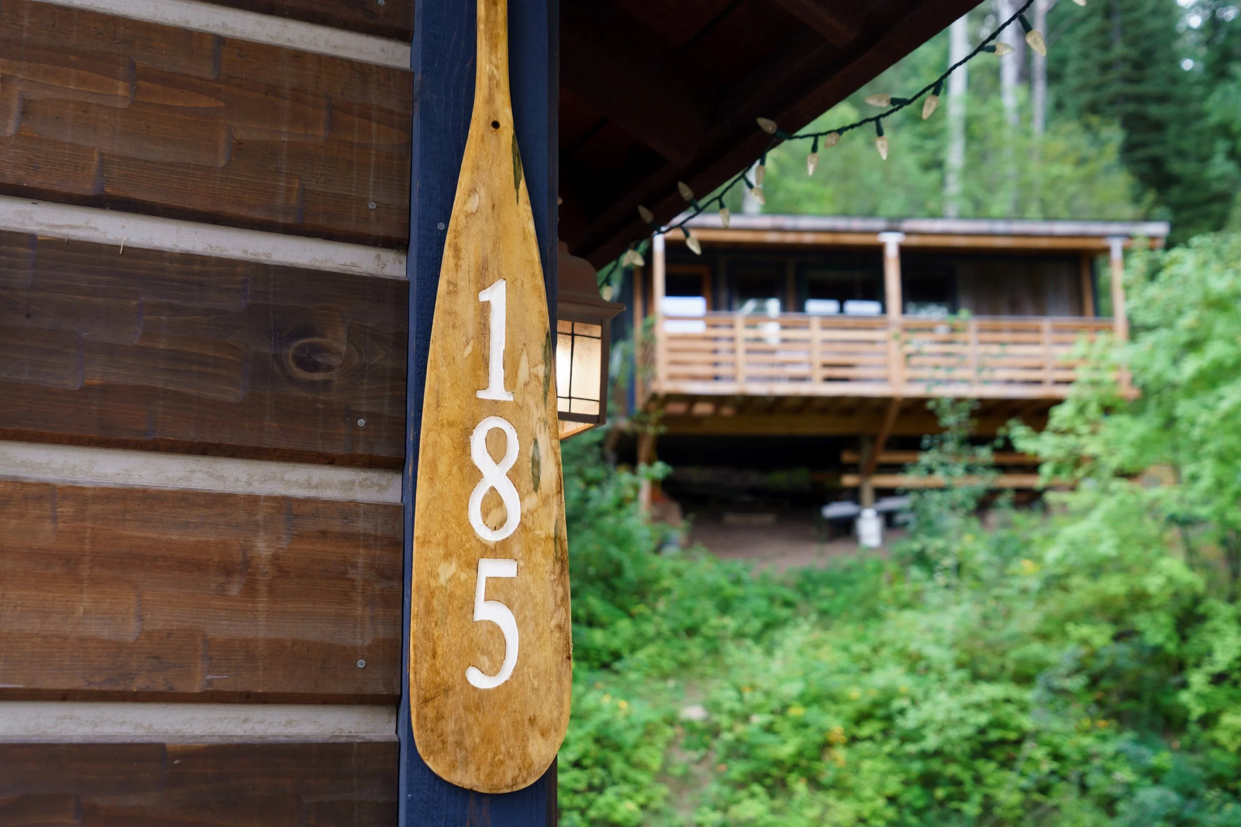 Wooden house with a rustic sign displaying the numbers 185, surrounded by lush green trees.