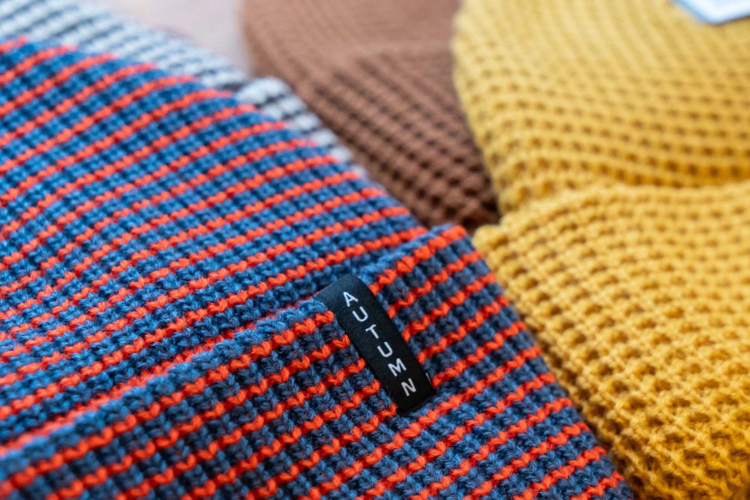 Close-up of a striped knit fabric with a black label reading 'AUXETIC', featuring red and blue stripes.