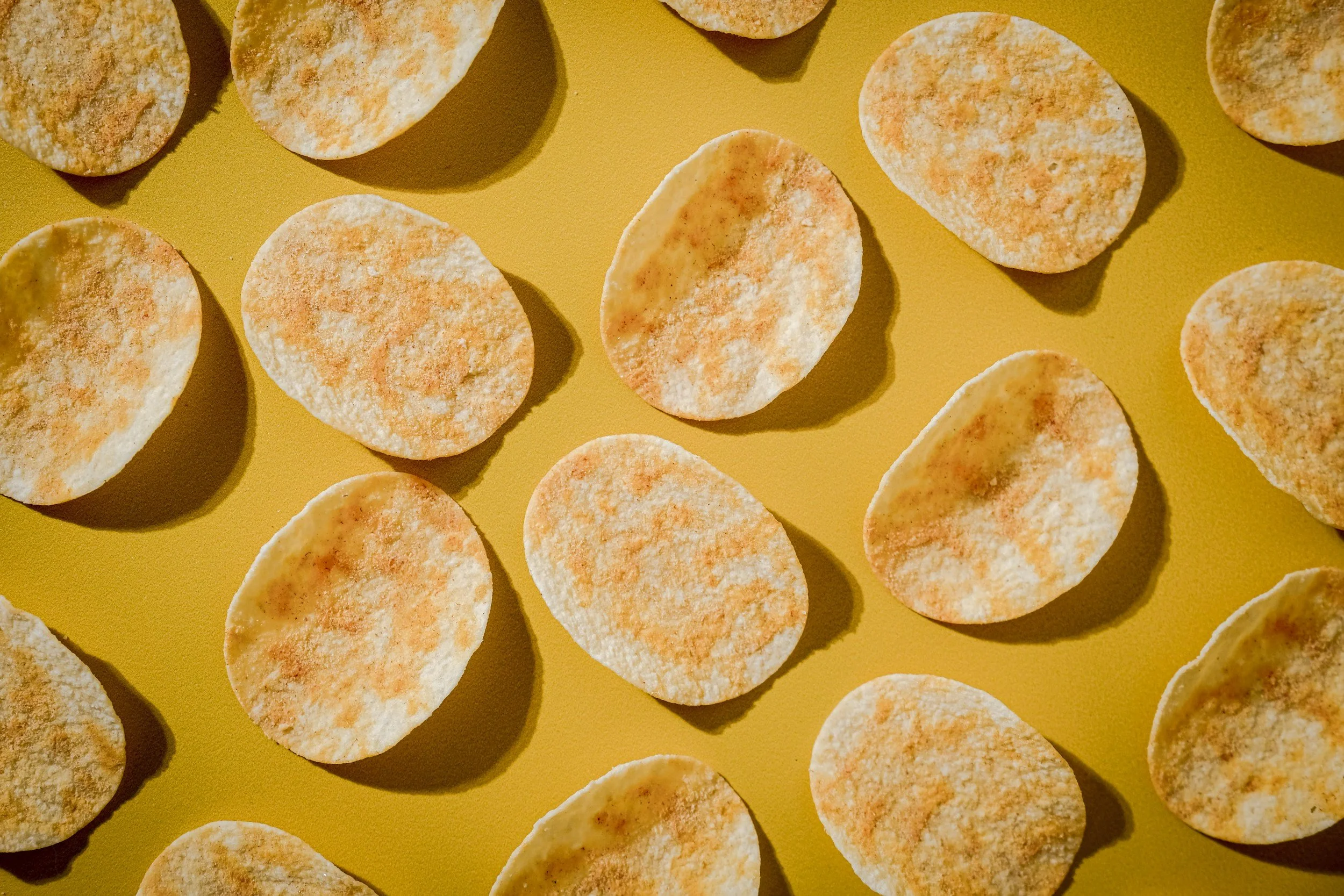 A mustard yellow surface holding ten individually spaced out seasoned potato chips.