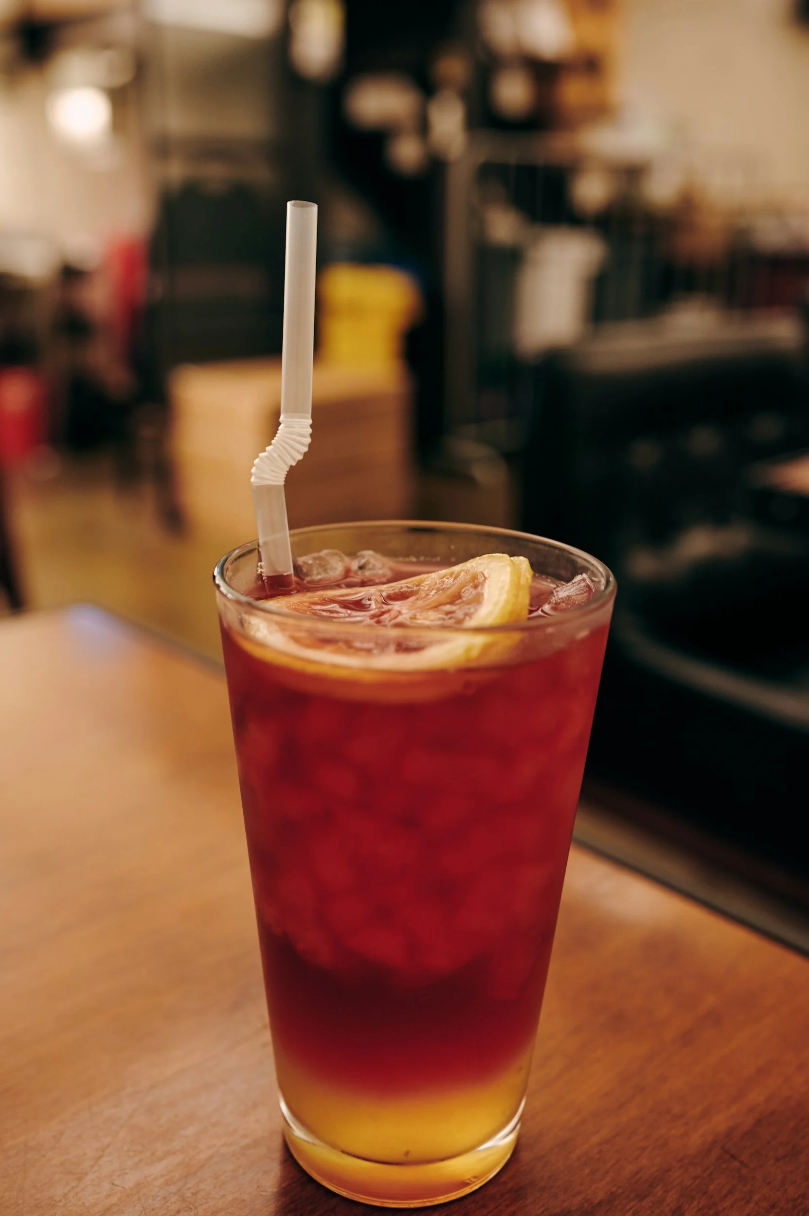 A pint glass with iced tea layered over lemonade, topped with a straw and a lemon wheel.