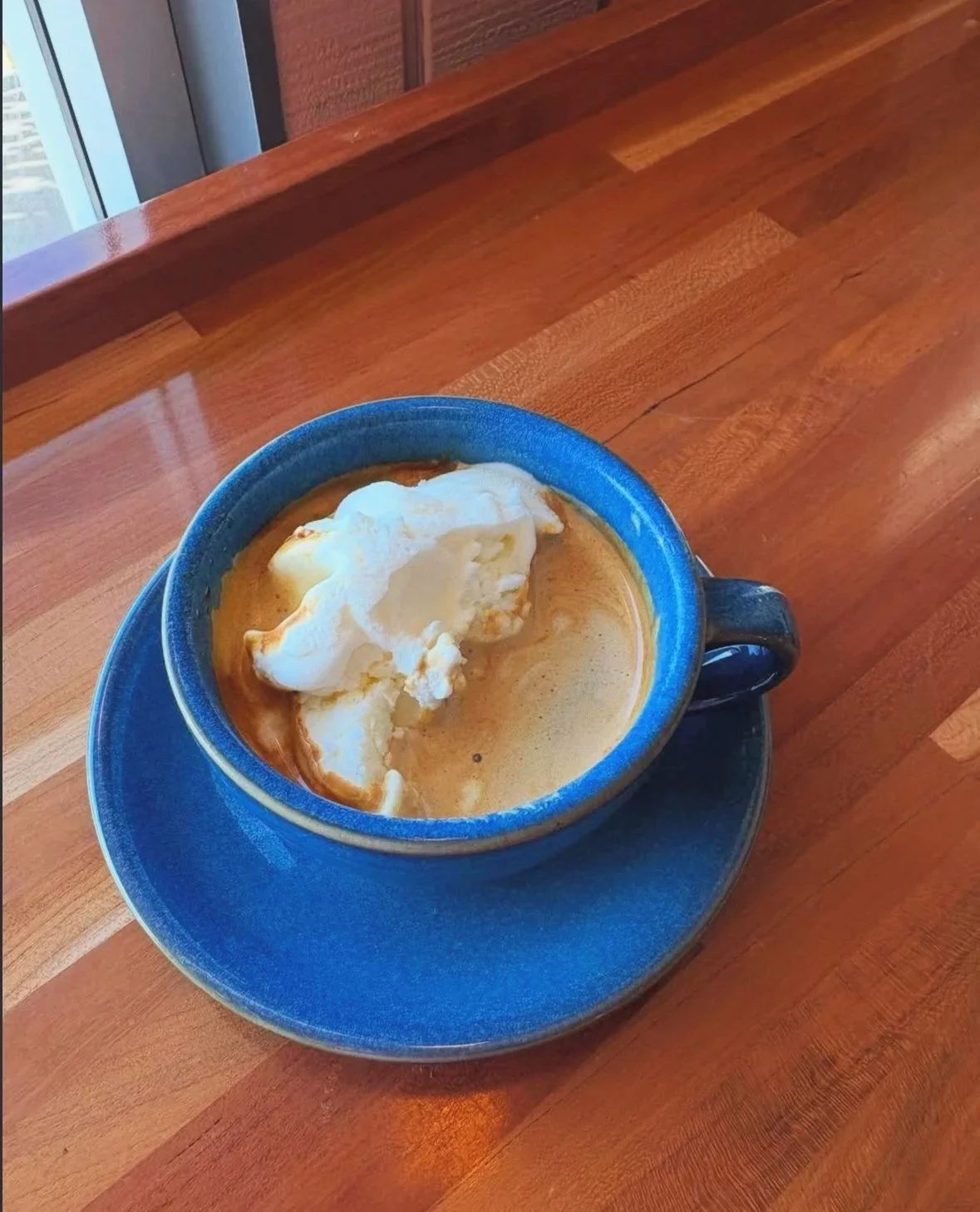 A small blue mug and saucer on a wooden countertop with vanilla ice cream and espresso.