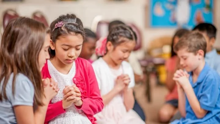 Group of young children praying together in a classroom.