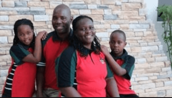 A family of five posing together in front of a brick wall. They are wearing matching red and black shirts.