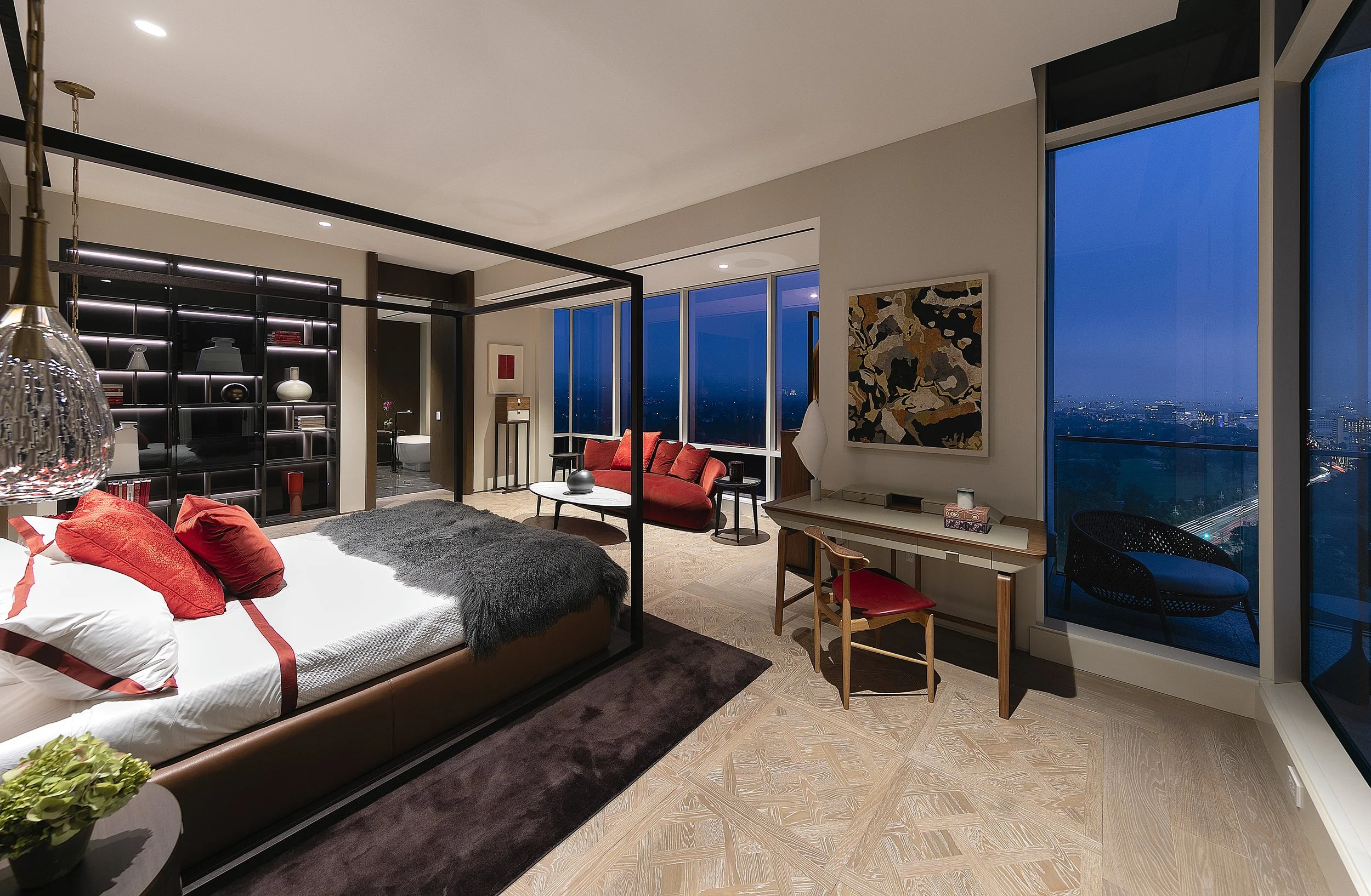 A modern city skyline visible through large floor-to-ceiling windows in a high-rise apartment living room during dusk or night, with lights illuminating the buildings.