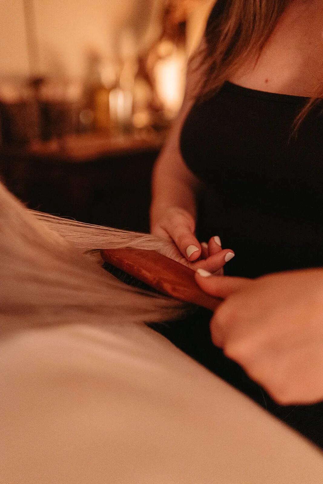 Close-up of a woman brushing a client's hair with a wooden brush in a warmly lit room.