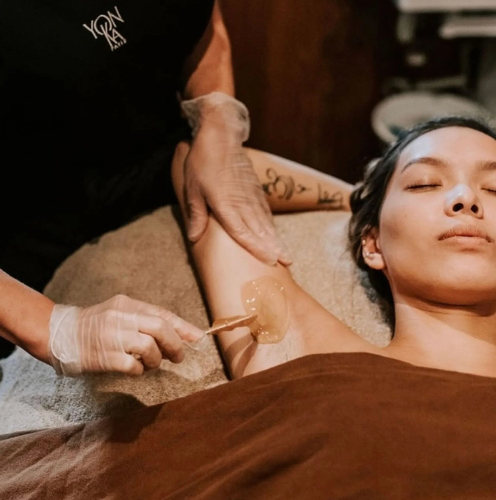 A woman on a treatment table receiving an underarm wax.