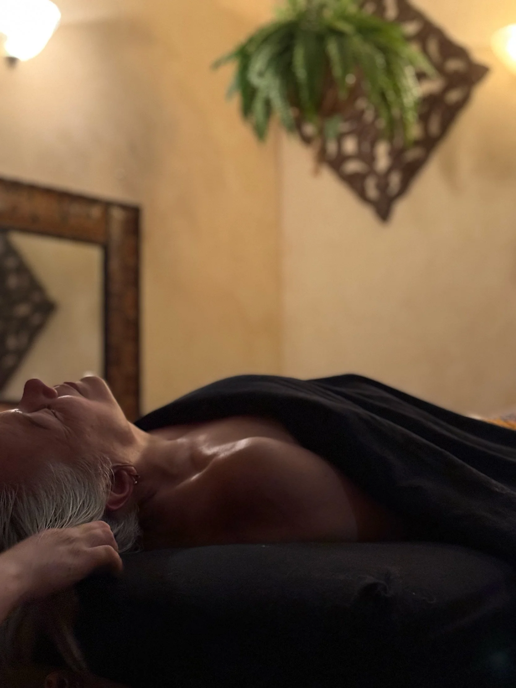 A woman with grey hair lying on a treatment table in a private spa treatment room.