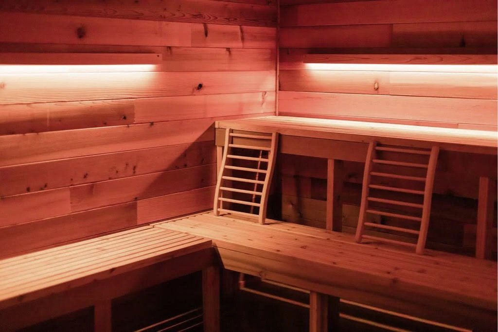 A wooden sauna interior with benches and a ladder, illuminated by soft red lighting.