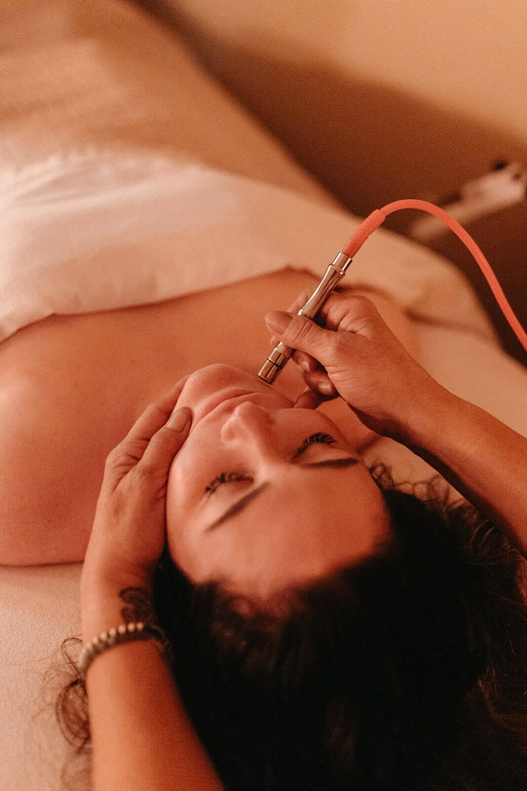 Person receiving a facial treatment, lying on a treatment table with their eyes closed.
