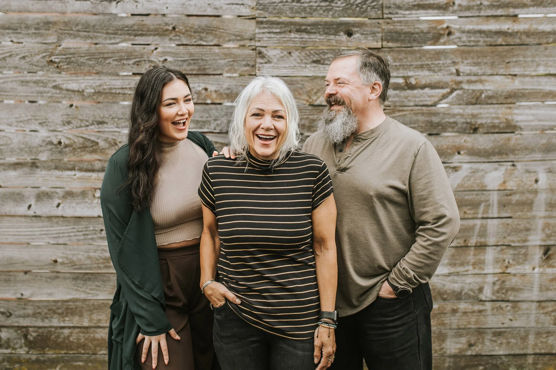 Spa Bliss owners standing together outdoors in front of a weathered wooden wall, smiling and enjoying each other's company.