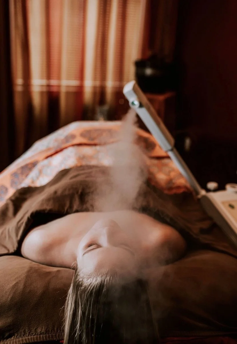 A person lying in bed with a blanket, having a steam facial with steam rising