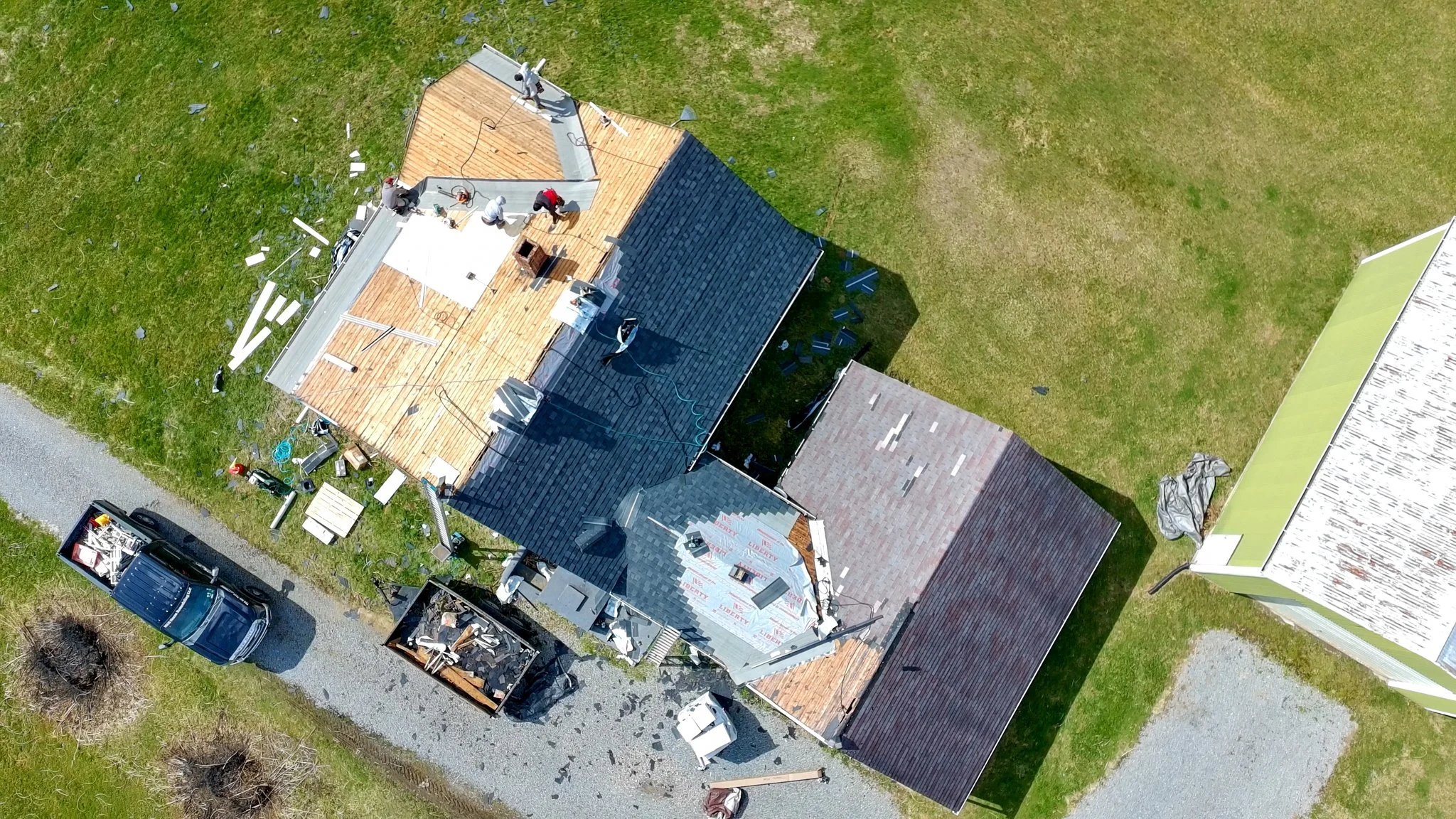 Two Pittsburgh roofers working outdoors, one with a white hoodie with a business logo and the other with a red hoodie, working on a roof repair project.