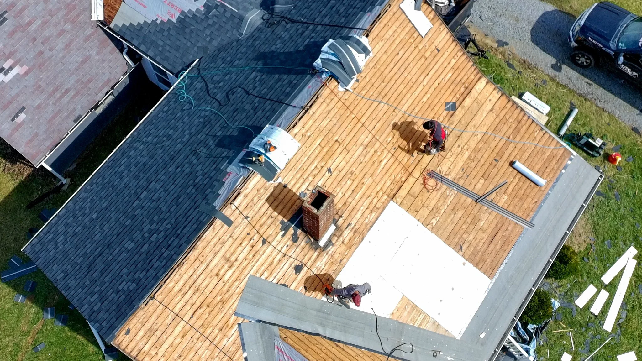 Two Pittsburgh roofers working outdoors, one with a white hoodie with a business logo and the other with a red hoodie, working on a roof repair project.