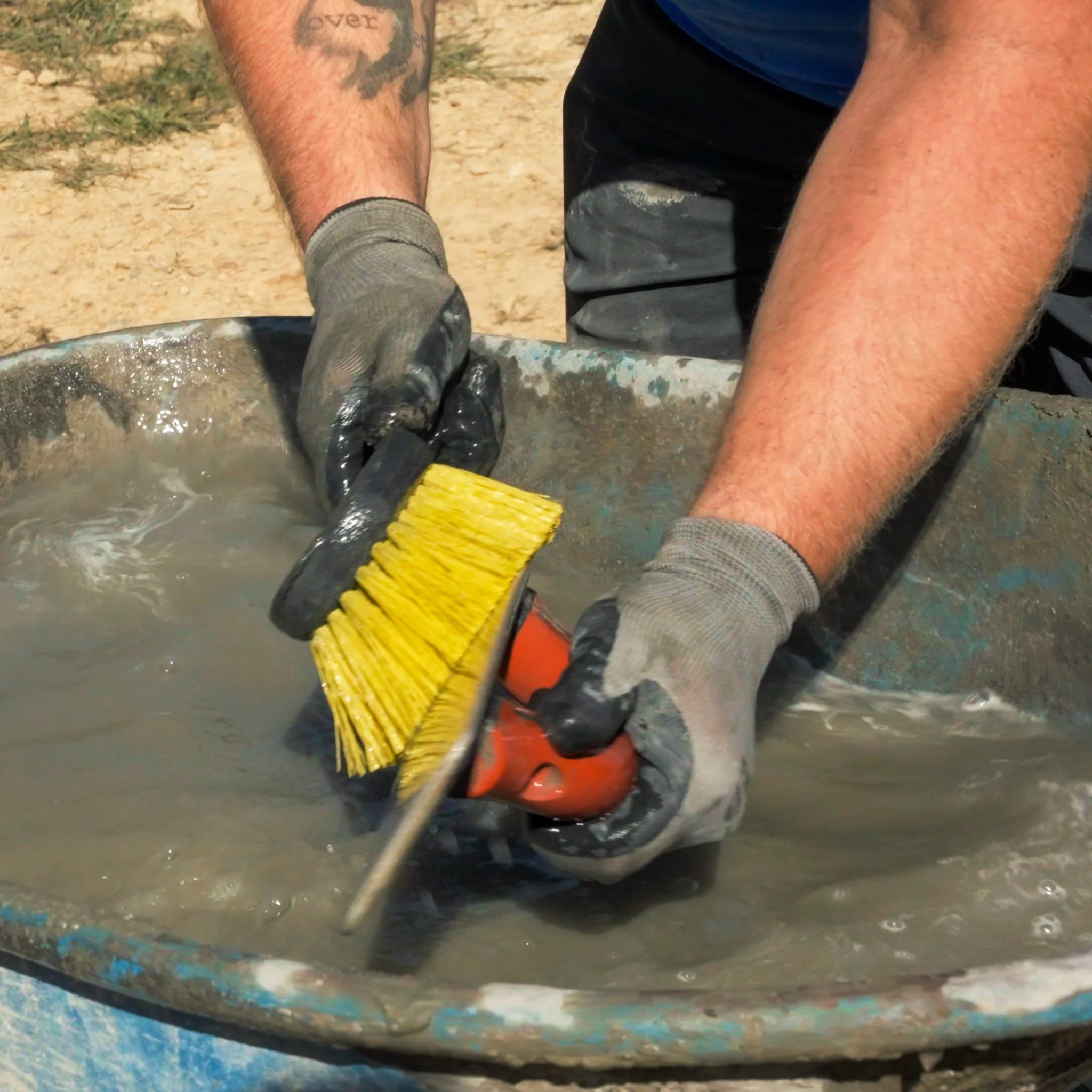 Pittsburgh contractor wearing gloves using a stiff scrub brush to clean a concrete surface in a wheelbarrow filled with muddy water.