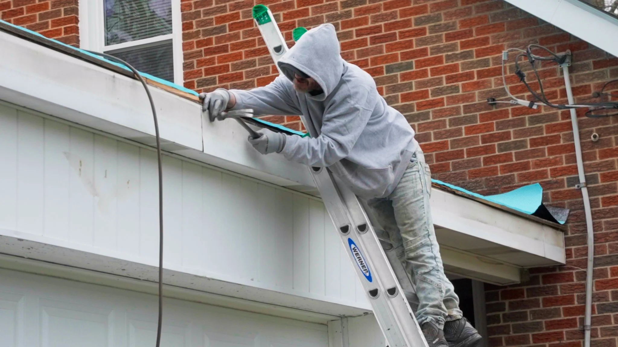 Pittsburgh roofers working outdoors, one with a white hoodie with a business logo and the other with a red hoodie, working on a roof repair project.