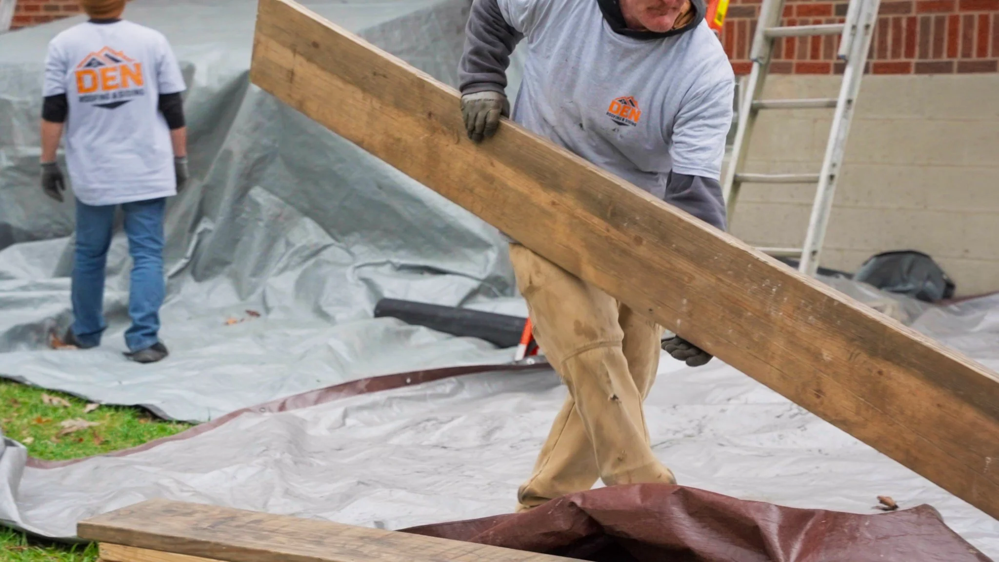 Pittsburgh roofers working outdoors, one with a white hoodie with a business logo and the other with a red hoodie, working on a roof repair project.