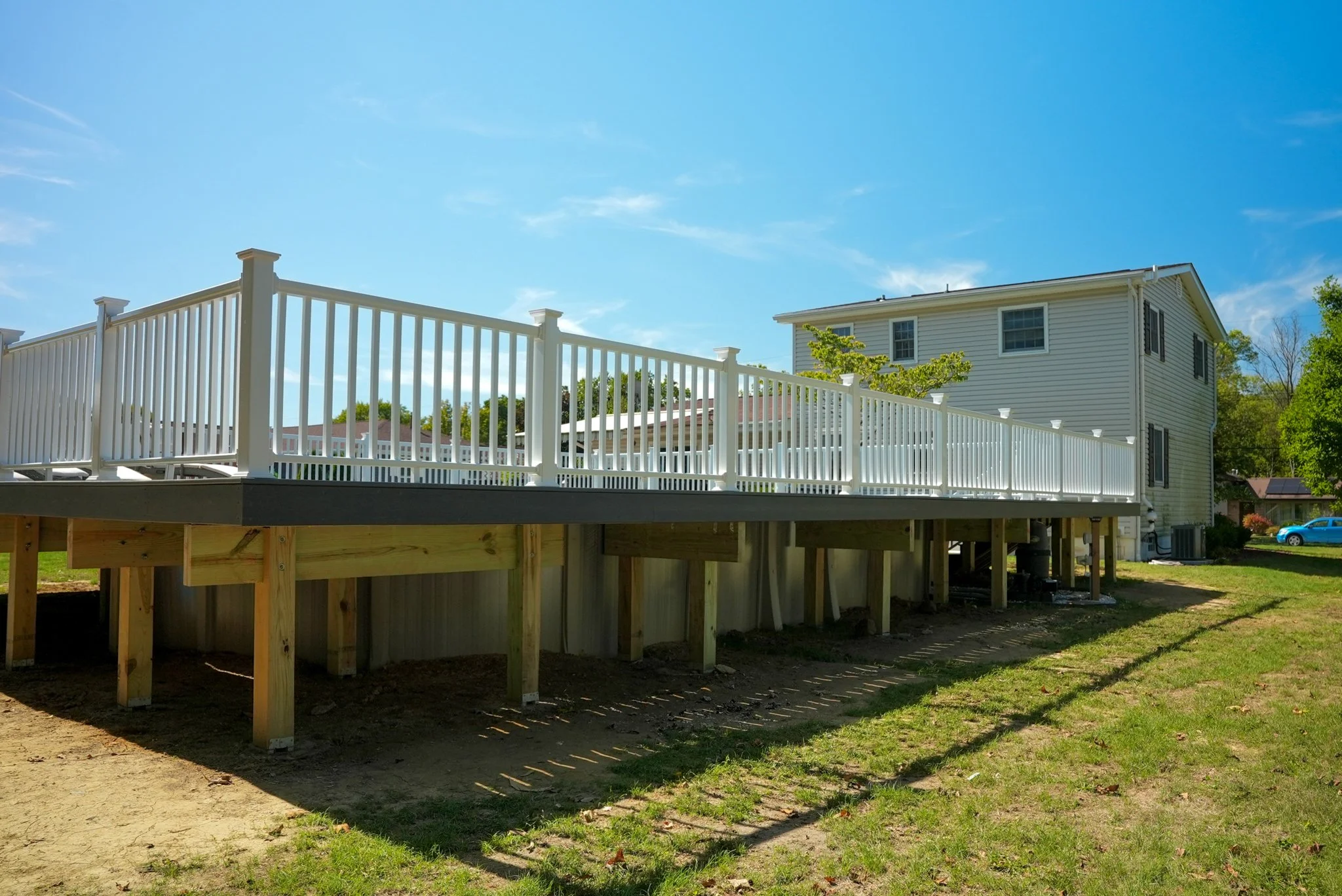 A newly built elevated deck with white railing, attached to a white house, under a clear blue sky.