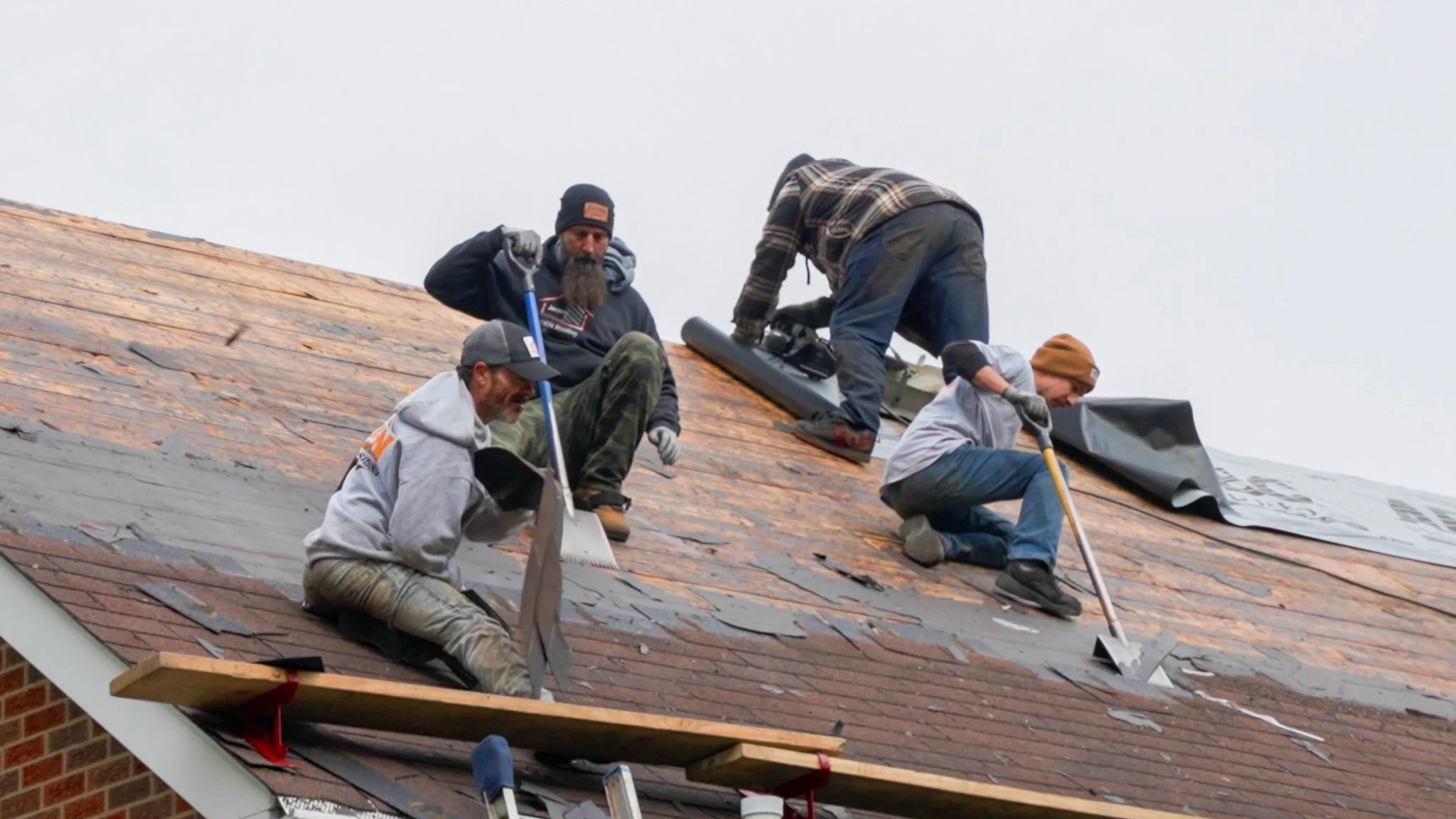 Pittsburgh roofers working outdoors, one with a white hoodie with a business logo and the other with a red hoodie, working on a roof repair project.
